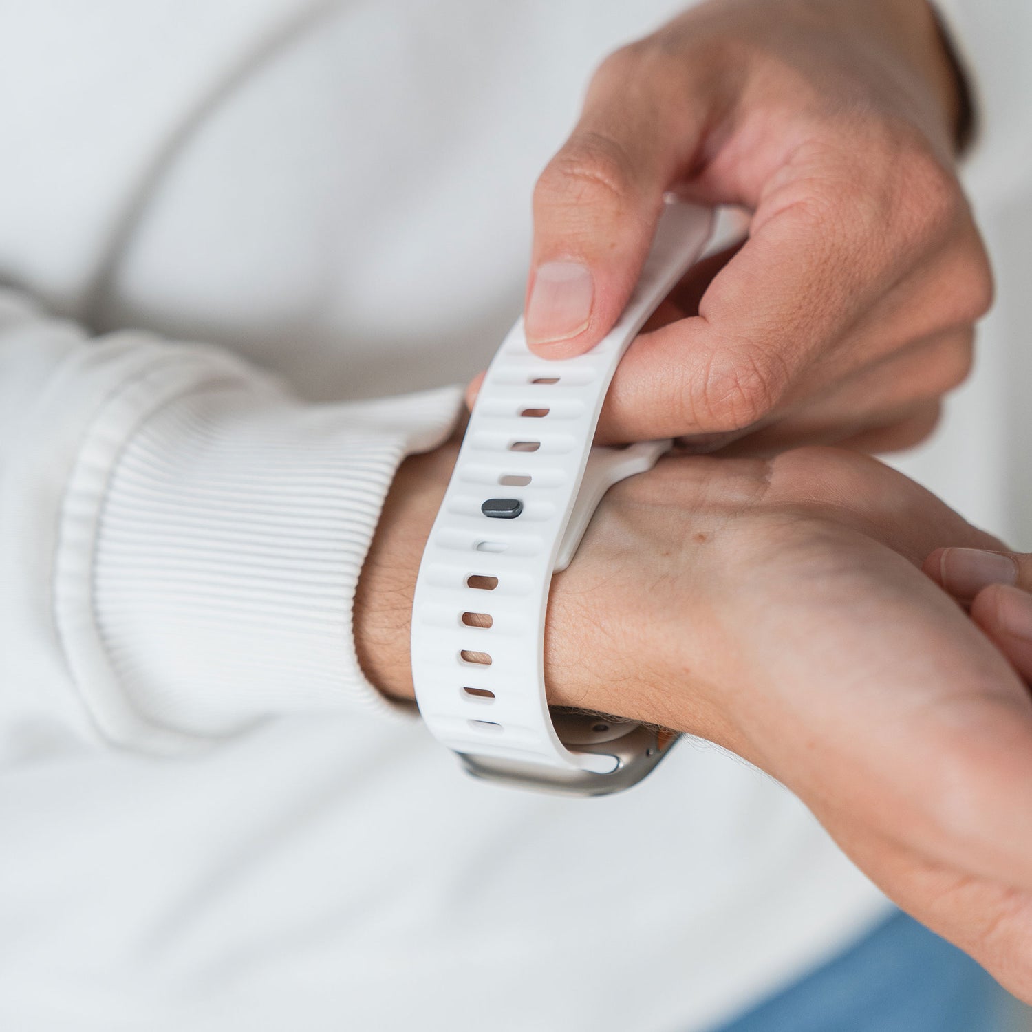 Eine Person in einem weißen Langarmshirt befestigt ein arktisband Apple Watch Silikonarmband „Active“ von arktisband an ihrem Handgelenk.