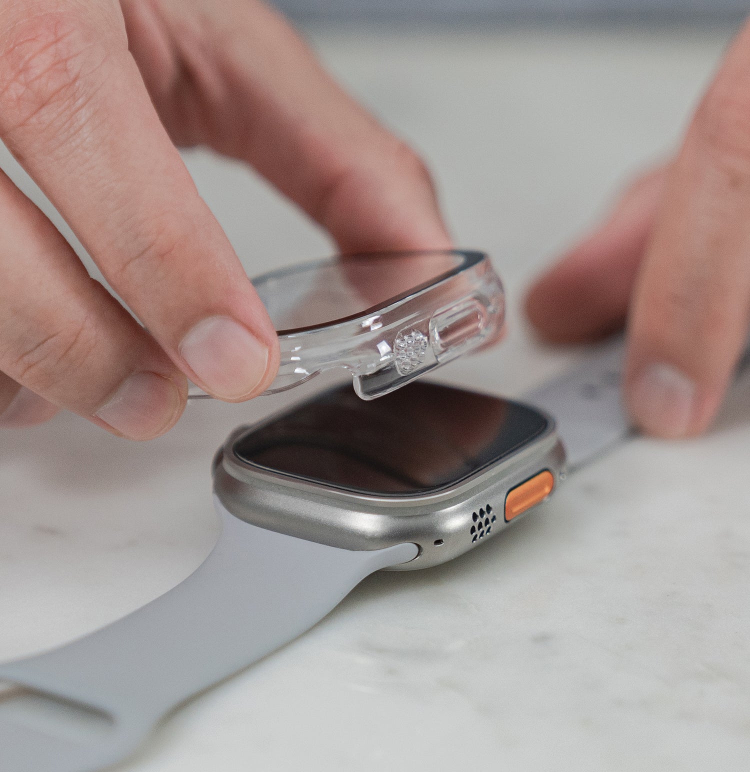 Eine Person legt eine durchsichtige Schutzhülle auf eine silberne Smartwatch mit grauem Armband.