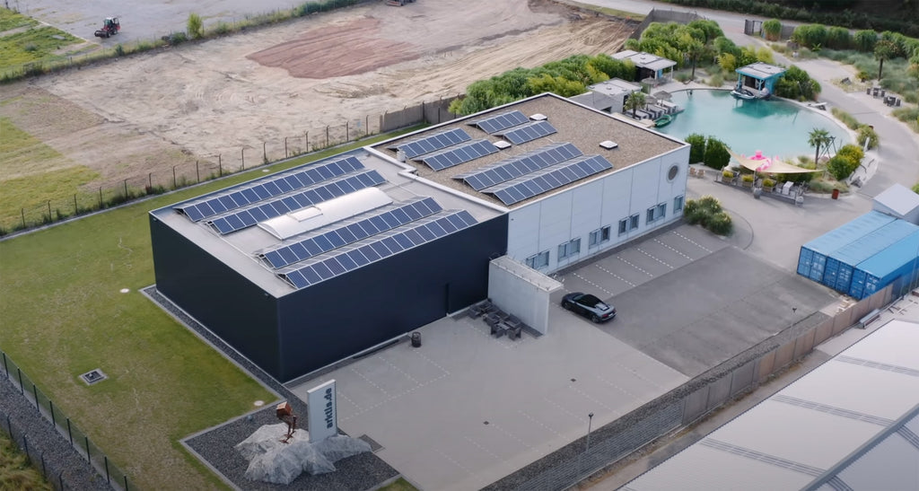 Luftaufnahme eines modernen Gebäudes mit Solarmodulen auf dem Dach und einem davor geparkten Auto.