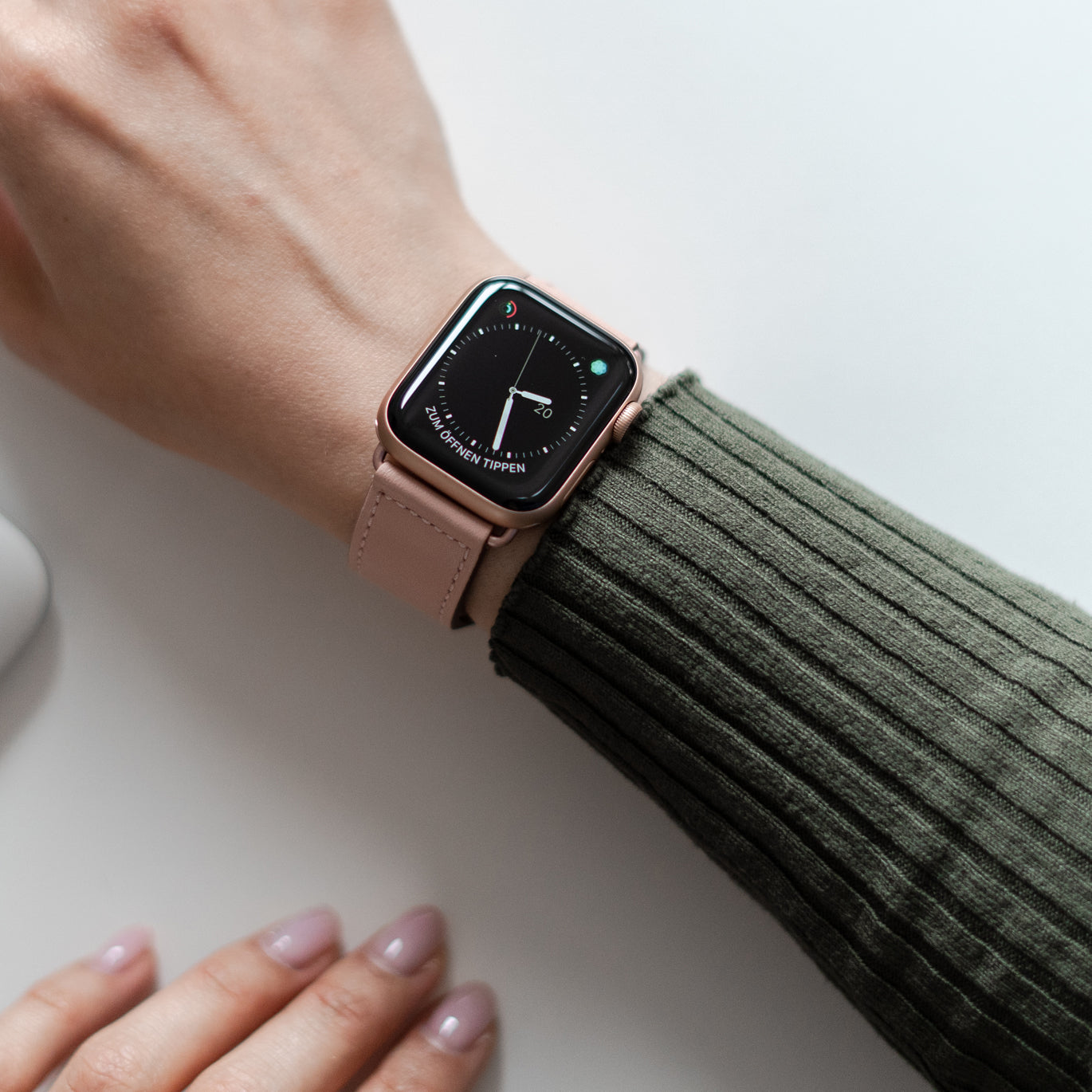 Von oben ist eine Person zu sehen, die eine Smartwatch mit rosa Armband und grünem Rippenärmel trägt.