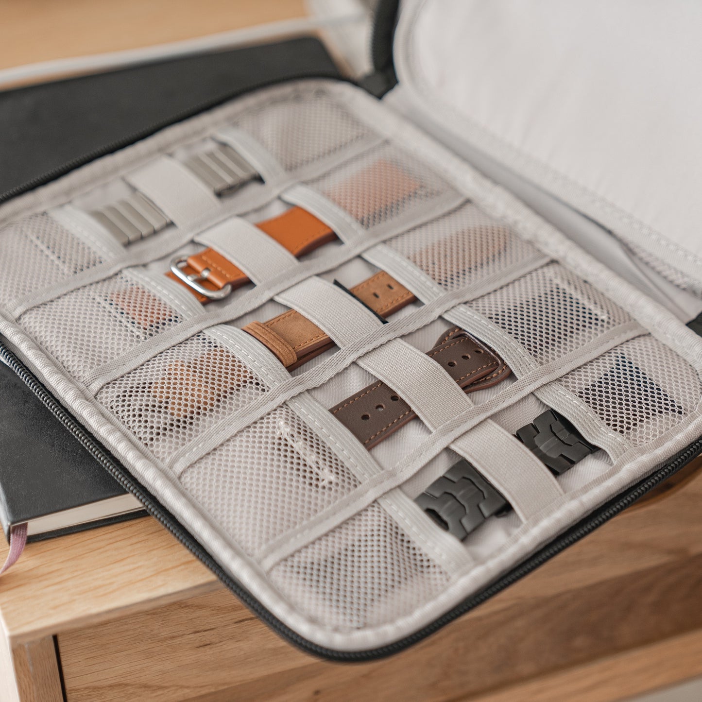 Die arktisband Kleine Reisetasche für Apple Watch Armbänder & Zubehör von arktisband lässt sich öffnen und enthüllt Netztaschen mit Apple Watch Armbändern in verschiedenen Farben und Materialien, die stilvoll auf einer Holzoberfläche angeordnet sind.