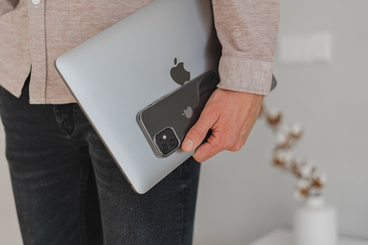 Person in Freizeitkleidung, die ein silbernes MacBook und ein schwarzes iPhone mit sichtbaren Apple-Logos hält.