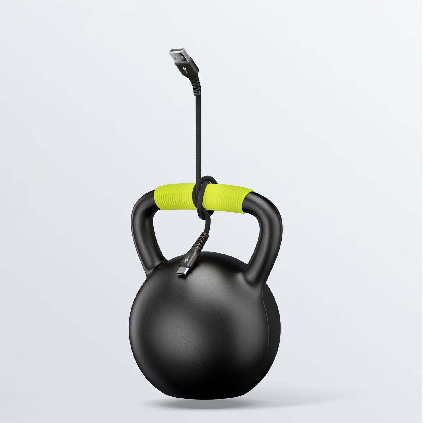 Eine schwarze Kettlebell mit grünen Griffen hängt an ihrem Griff an einem Goobay USB-C auf USB-A Textilkabel mit Metallsteckern vor einem schlichten hellen Hintergrund. Der USB-Stecker ist oben im Bild sichtbar.