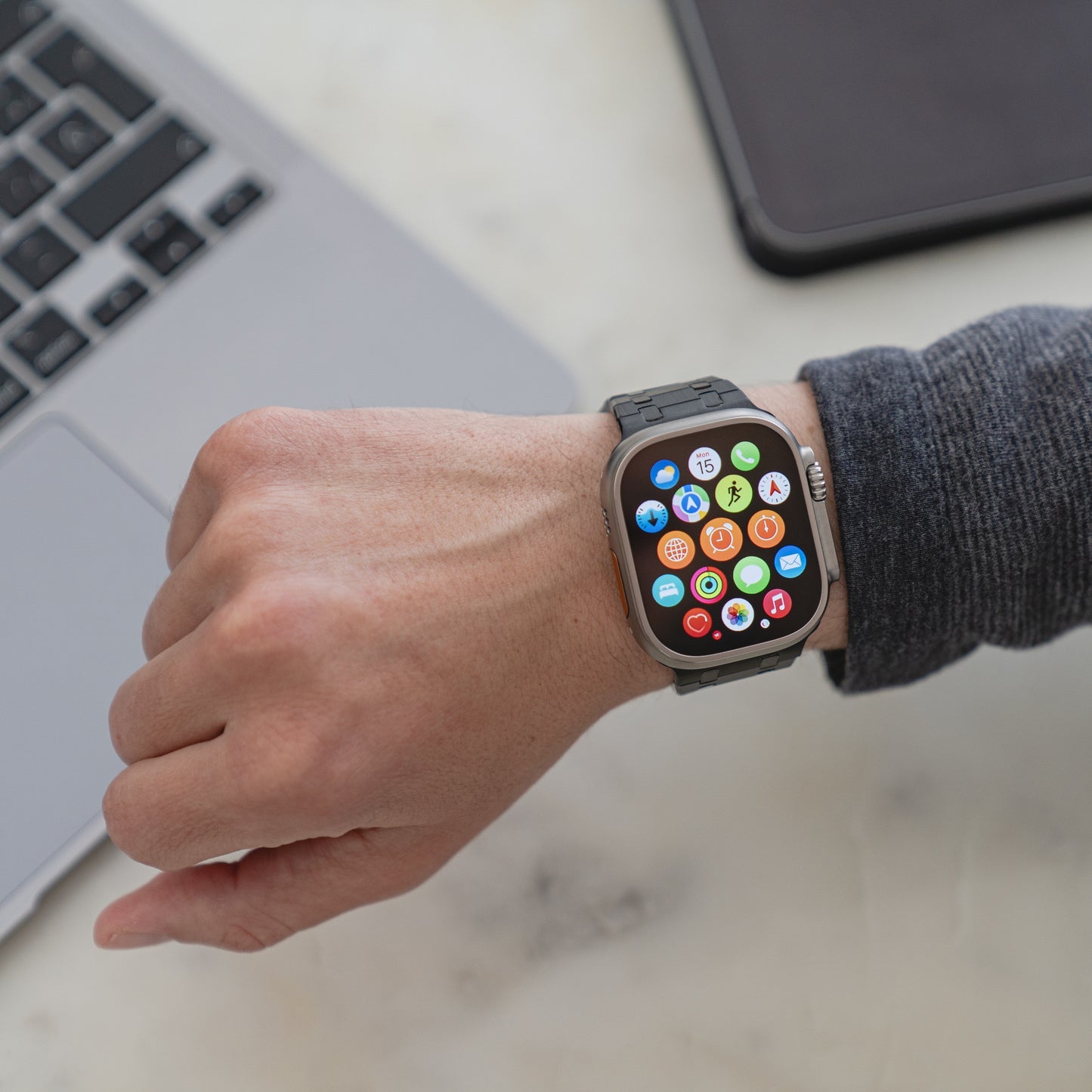 Jemand trägt das Arktisband Edelstahlarmband „Symphony“ für die Apple Watch mit bunten App-Symbolen und sitzt neben einem Laptop auf einem Schreibtisch.