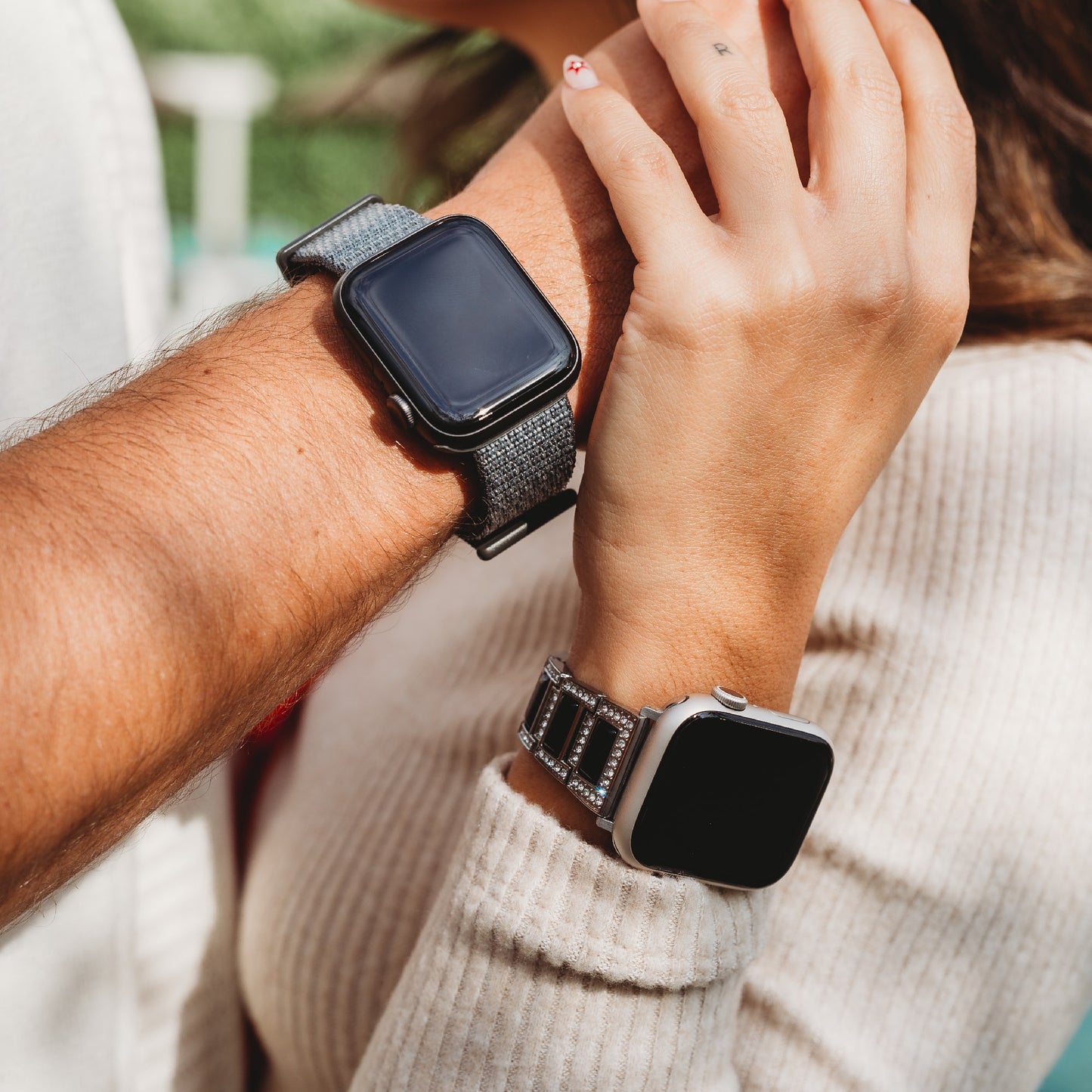 Zu sehen sind die Handgelenke zweier Personen, die jeweils ein arktisband Apple Watch Armband tragen – eine mit dunklem Stoffarmband, die andere mit dem arktisband Apple Watch Gliederarmband „Senorita“ mit Strasssteinen. Beide Uhrenbildschirme sind ausgeschaltet.