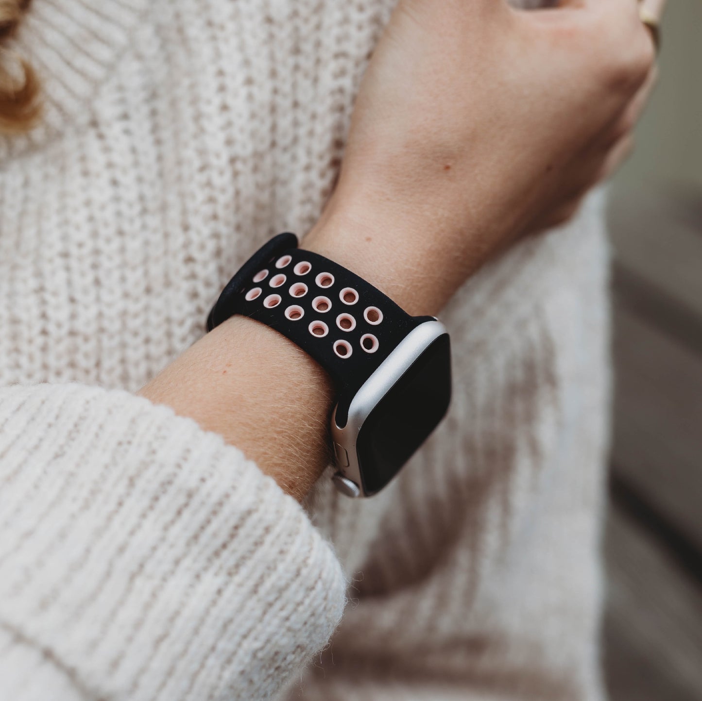 Eine Person trägt einen cremefarbenen Strickpullover und ein arktisband Apple Watch Silikonarmband „Energy“, ein schwarz-pinkes perforiertes Band von arktisband, am Handgelenk.