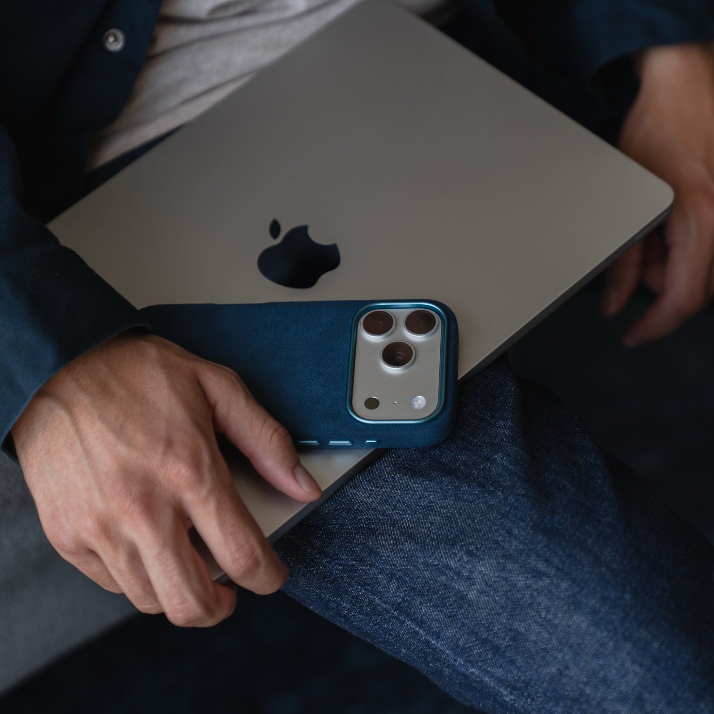 Eine Person hält ein silbernes MacBook und eine blaue arktis iPhone 17 Pro Hülle aus Alcantara, made in Italy, während sie in Jeans und einem Hemd sitzt.