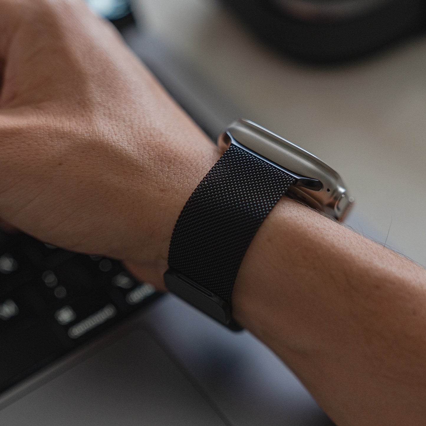 Eine Nahaufnahme eines Handgelenks mit dem schwarzen Arktisband Apple Watch Milanaise Loop Armband von Arktisband, das auf einer Tastatur ruht. Das Zifferblatt ist nicht sichtbar.
