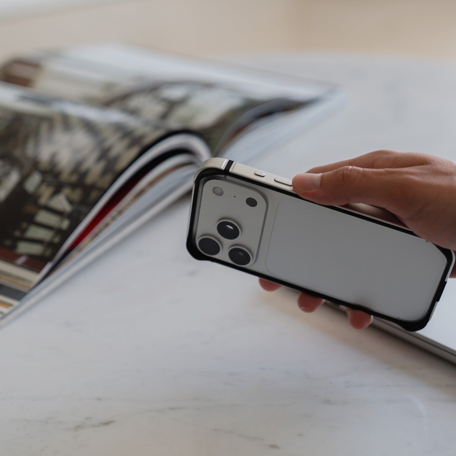 Eine Hand hält einen arktis iPhone 17 Pro Bumper von arktis neben einem offenen Magazin auf einer weißen Fläche.