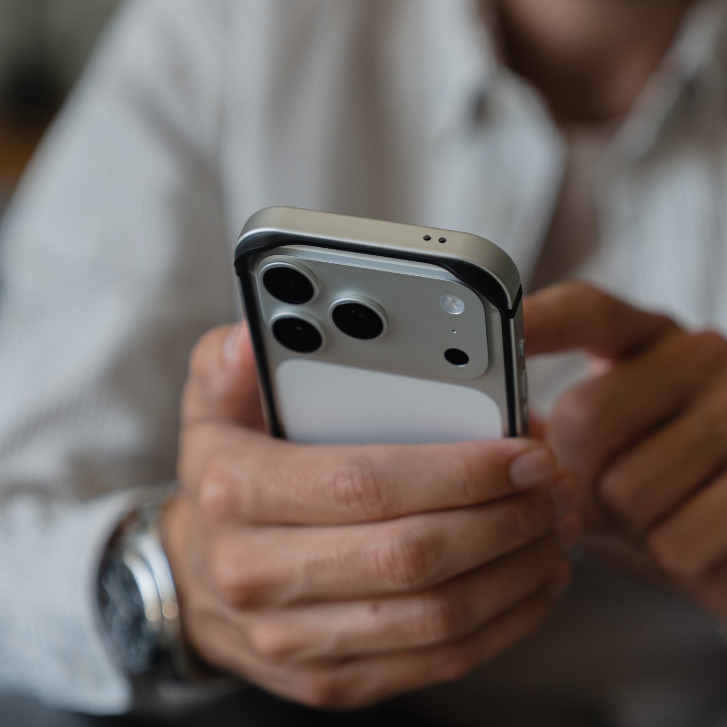 Eine Person, die ein Smartphone mit drei Kameras benutzt, trägt ein gestreiftes Hemd und einen arktis iPhone 17 Pro Bumper - eine ultraleichte Aluminium-TPU-Silikonhülle von arktis.