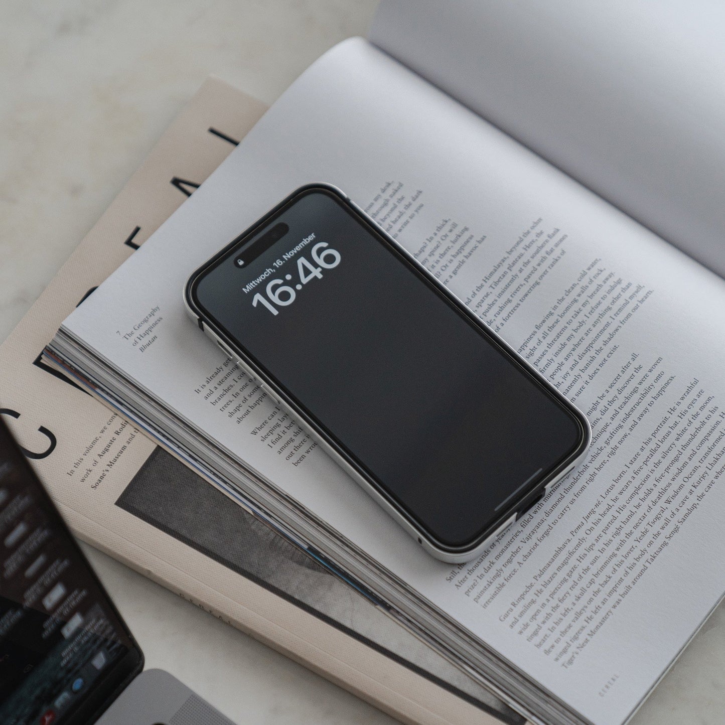 Aviato’s AirZERO Alu Bumper für iPhone 15 Pro Max aus Flugzeugaluminium schützt und veredelt das Smartphone, das kabellos auf ein offenes Buch und Magazin geladen wird.