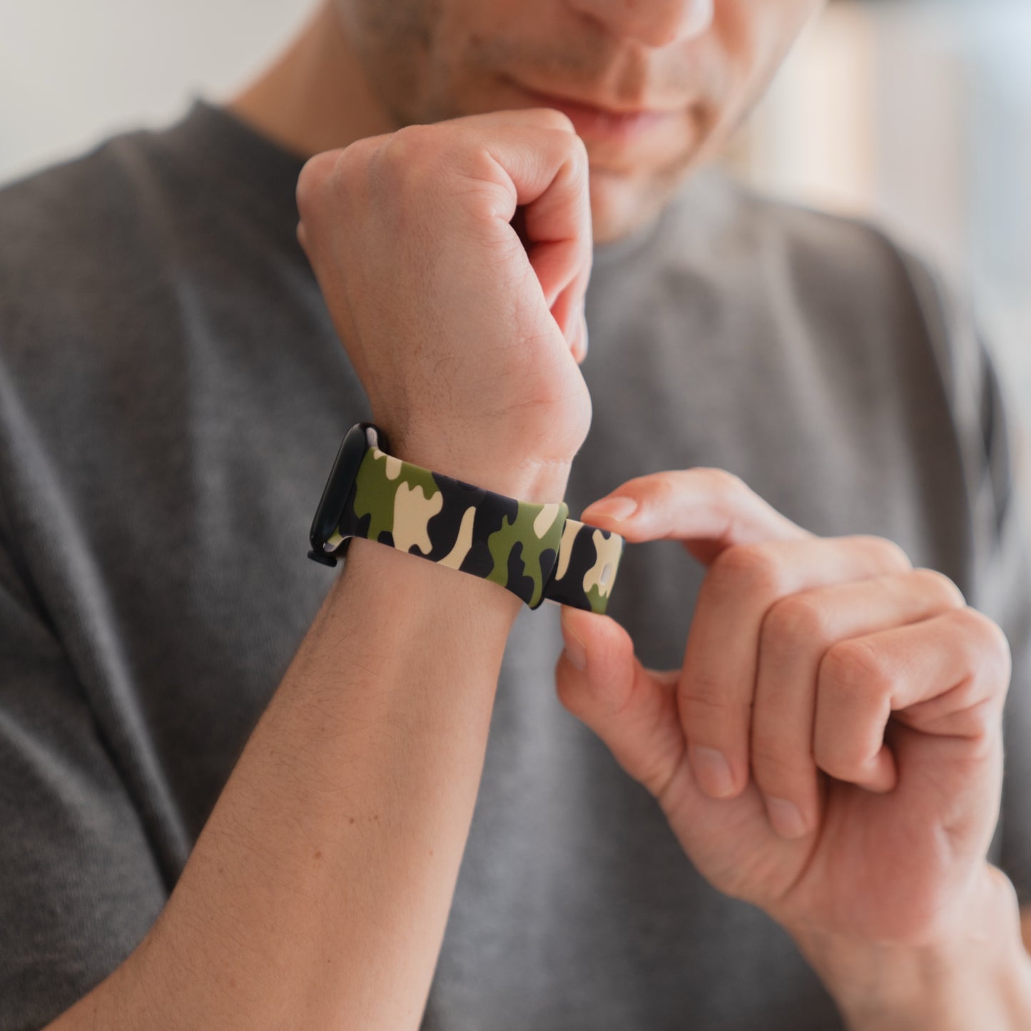 Ein Mann in einem grauen Hemd passt sein arktisband Camouflage Apple Watch Armband, ein sportliches und stilvolles Accessoire von arktisband, an seinem Handgelenk an.