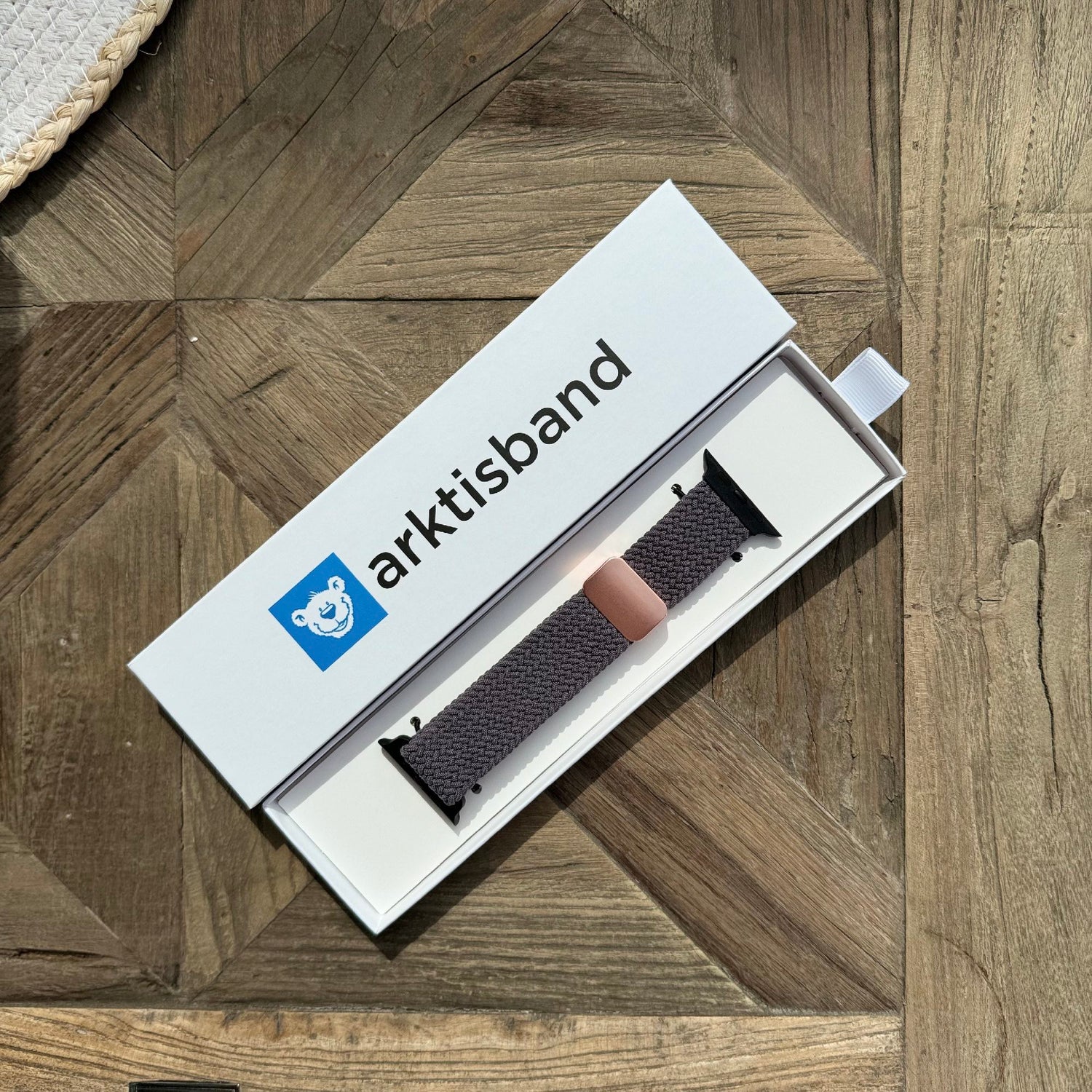 Ein verpacktes arktisband Geflochtenes Apple Watch Armband „Casual“ mit Magnetverschluss liegt auf einem Holztisch und ist bereit, Ihre arktisband Smartwatch-Armbandkollektion aufzuwerten.