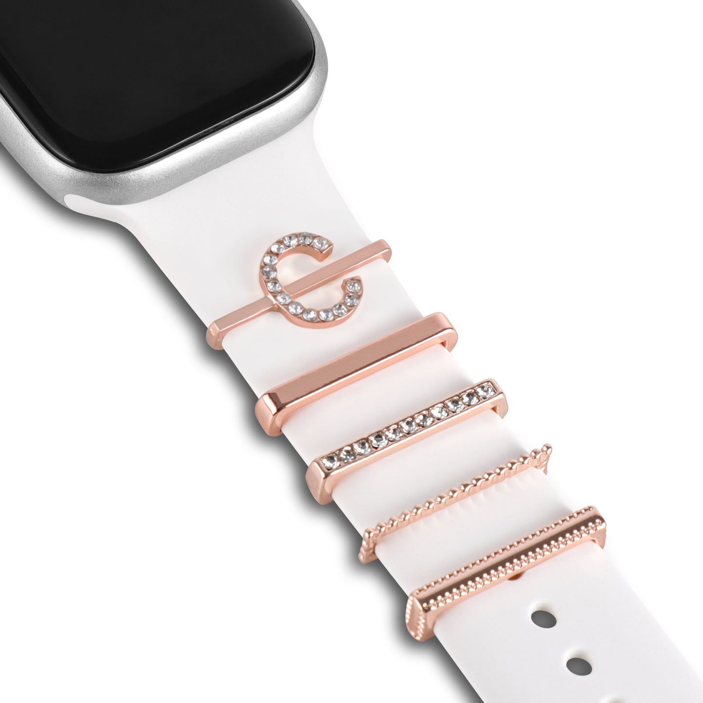 Eine Nahaufnahme eines weißen arktisband Apple Watch Armbands mit fünf dekorativen Charms „C Style“ von arktisband in Roségold, darunter ein Buchstabe C und vier Bars mit funkelnden Steinen. Das schwarze Zifferblatt ist teilweise sichtbar.