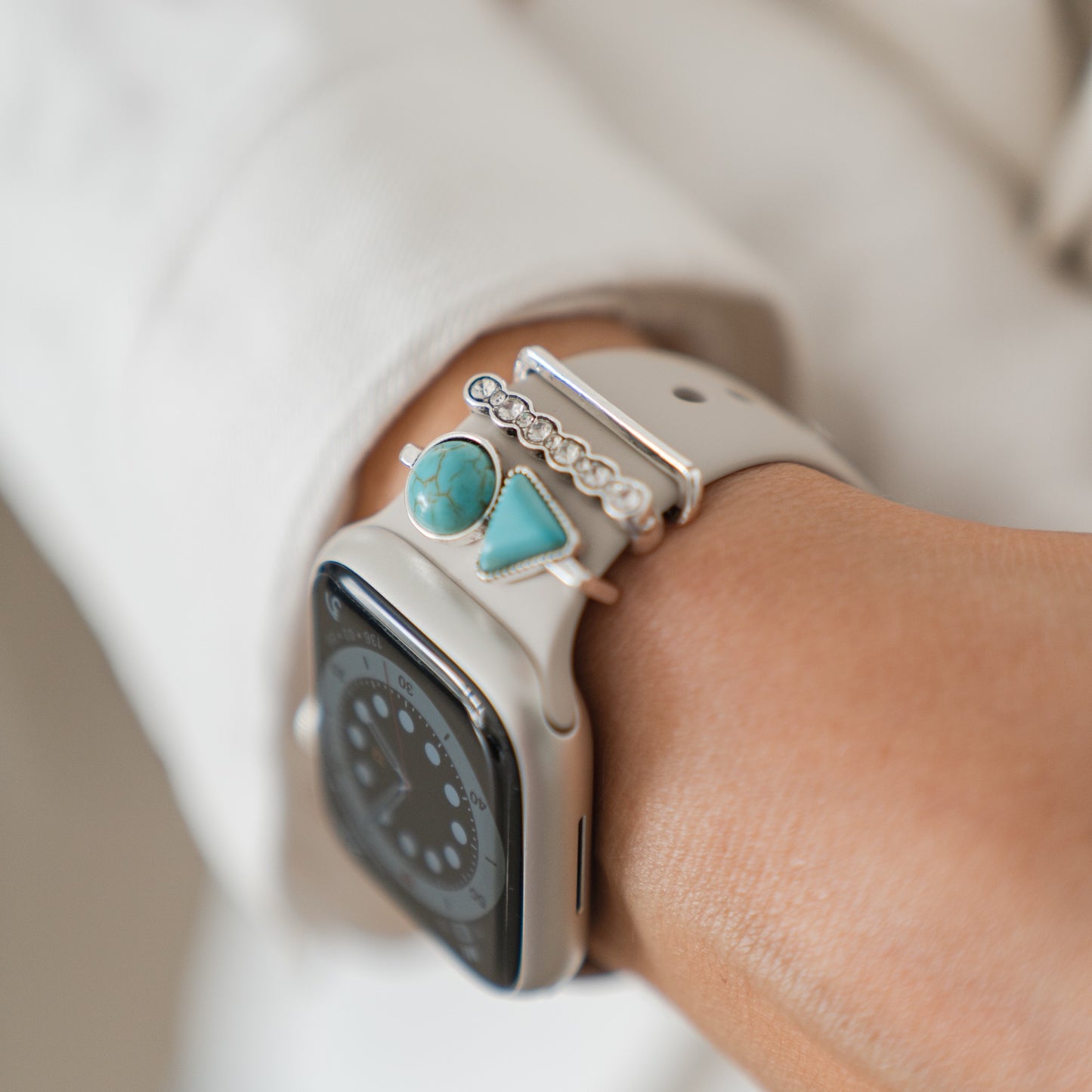 Die arktisband Apple Watch Charms "Opal" – Silber von arktisband aus Edelstahl und Glas zieren ein weißes Smartwatch-Armband mit türkisfarbenen und silbernen Ringen und tragen sich stilvoll am Handgelenk.