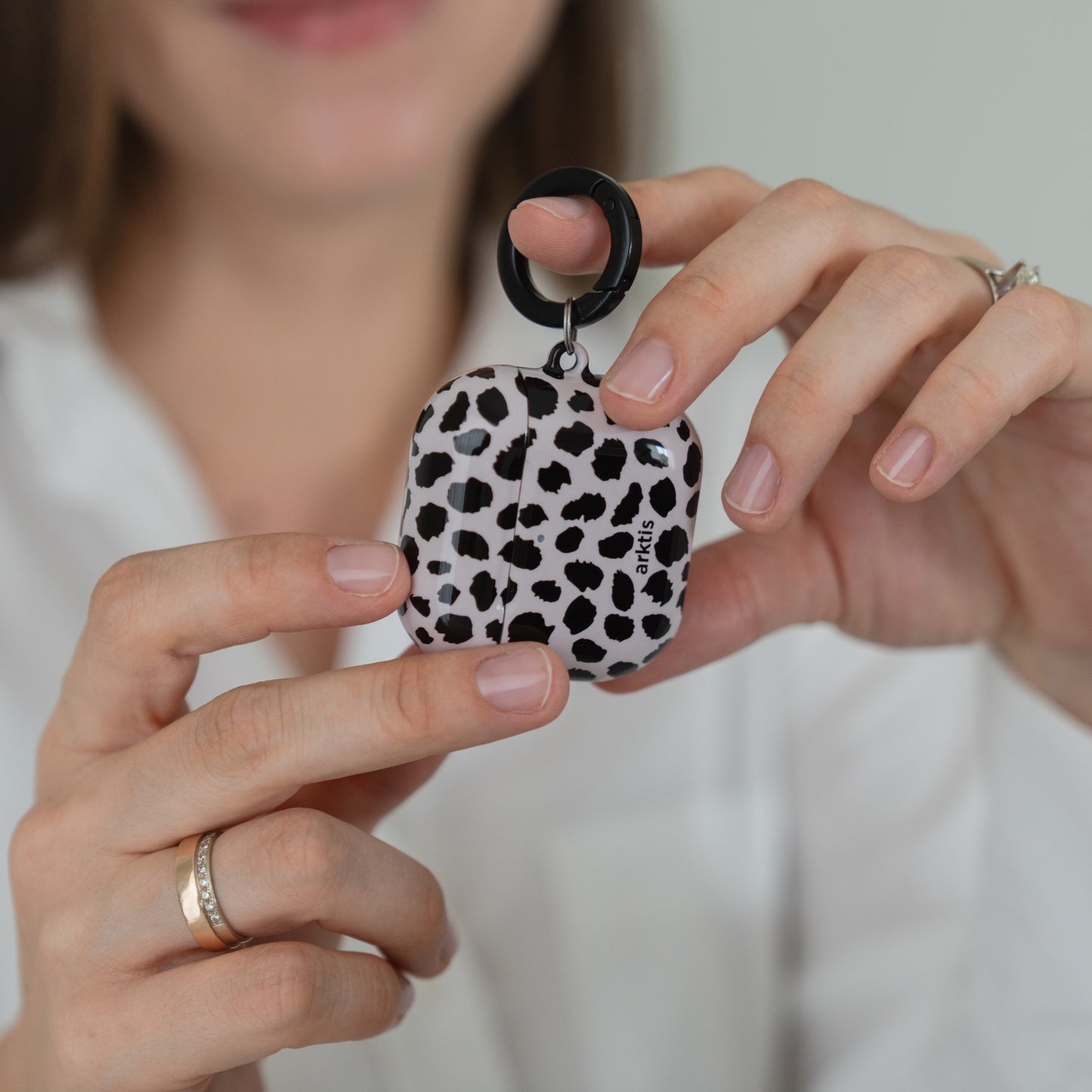 Hände, die eine Arktis AirPods 5-Hülle – Cheetah-Hülle mit schwarzem Ringaufsatz – halten.