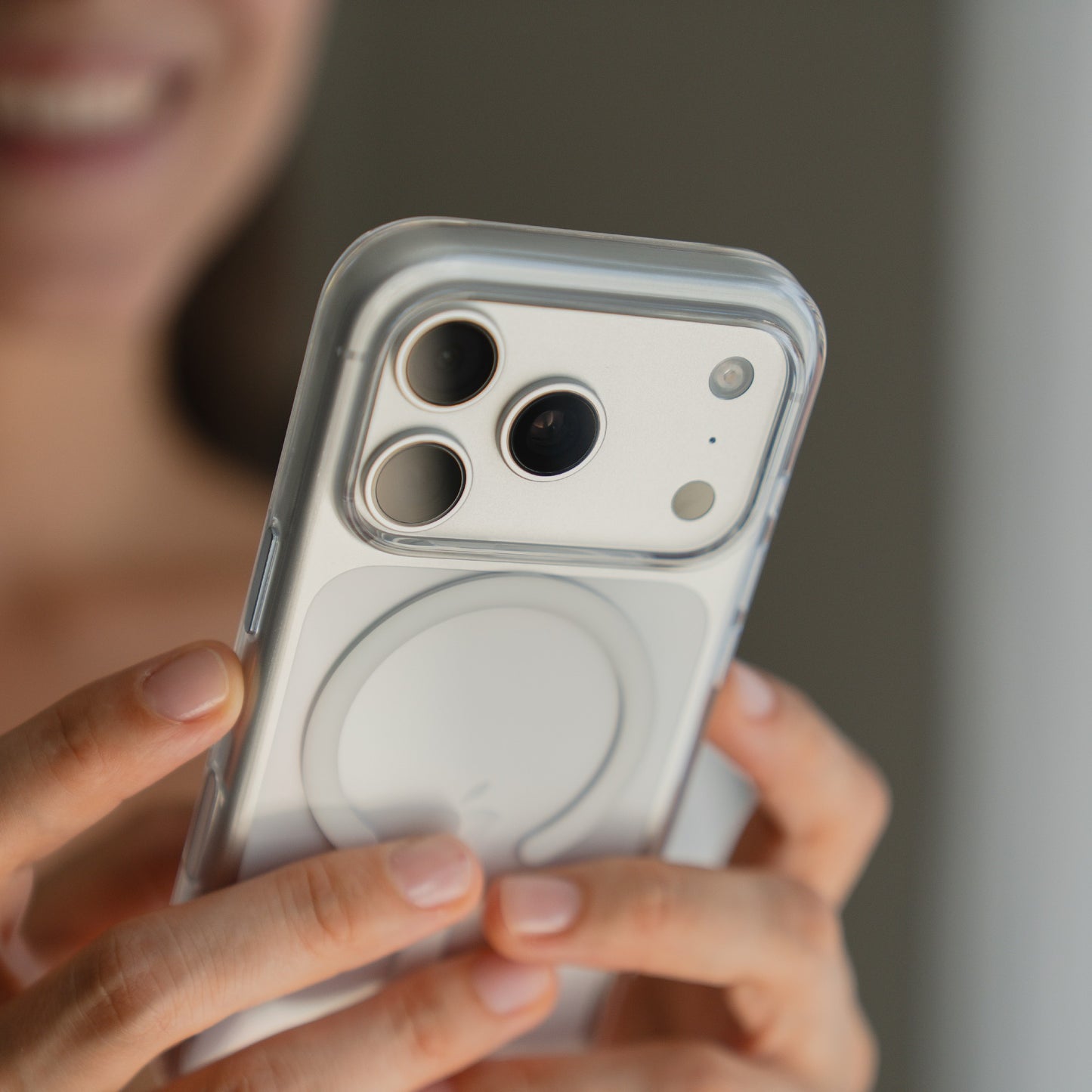 Eine Person hält ein arktis iPhone 17 Pro Max PureCase mit MagSafe Transparent Case auf einem weißen iPhone und lächelt im Hintergrund.