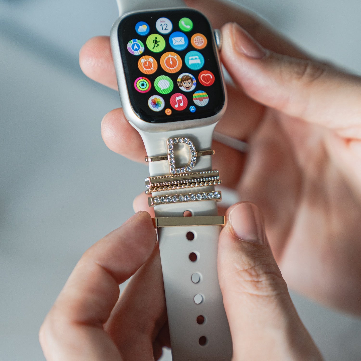 Eine Person hält eine Apple Watch mit stylischen Arktisband Apple Watch Charms „D Style“, die das weiße Arktisband-Armband zieren.