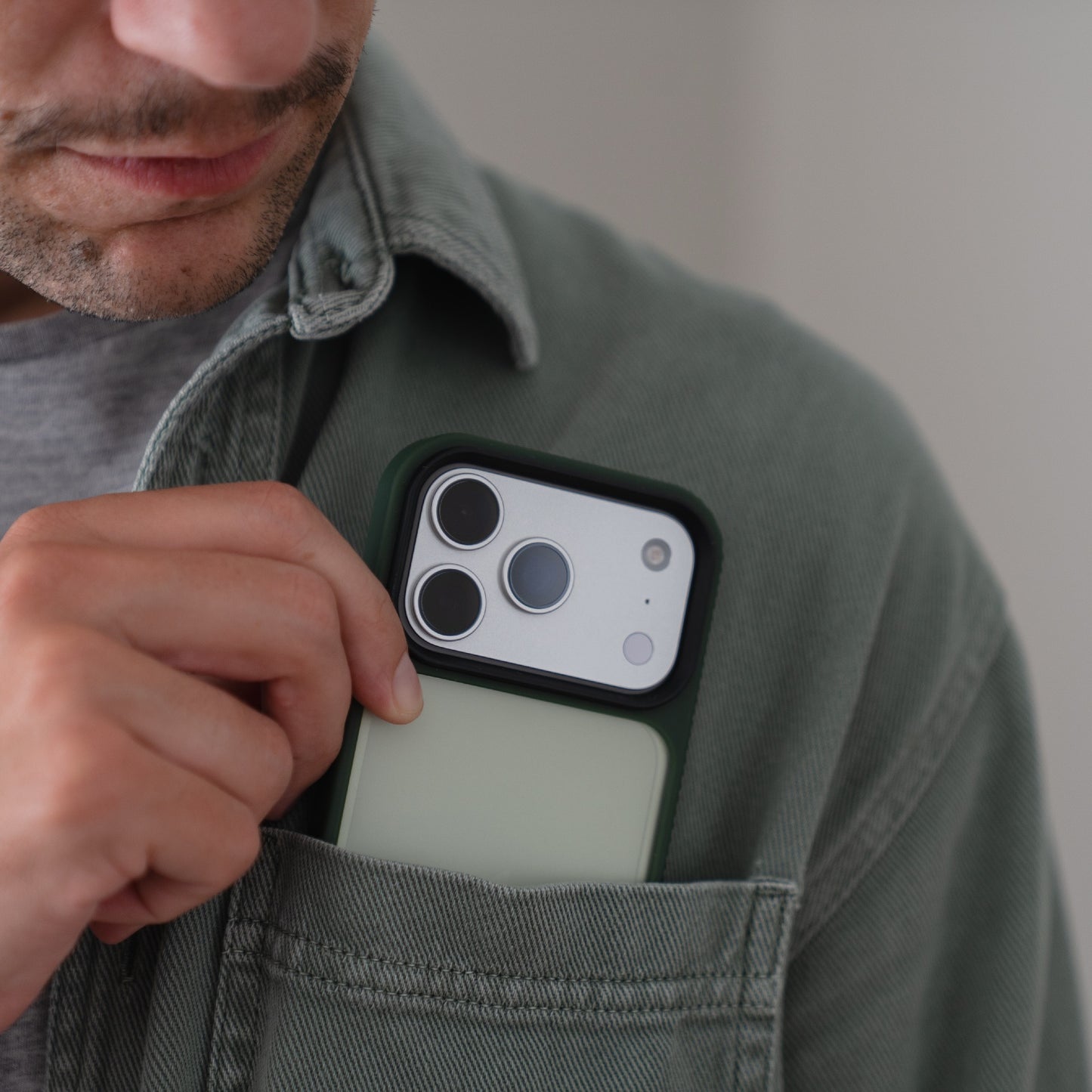 Ein Mann steckt ein arktis iPhone 17 Pro Solid Case von Arktis in die Brusttasche seines grünen Hemdes.
