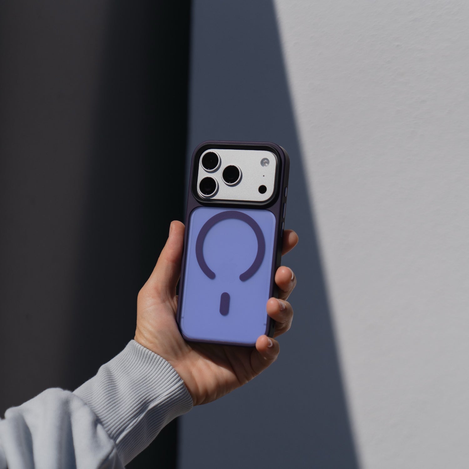 Eine Hand hält ein Arktis iPhone 17 Pro Solid Case mit MagSafe auf einem Smartphone, mit einem lila MagSafe kompatiblen Akkupack, vor einem weißen und grauen Hintergrund.