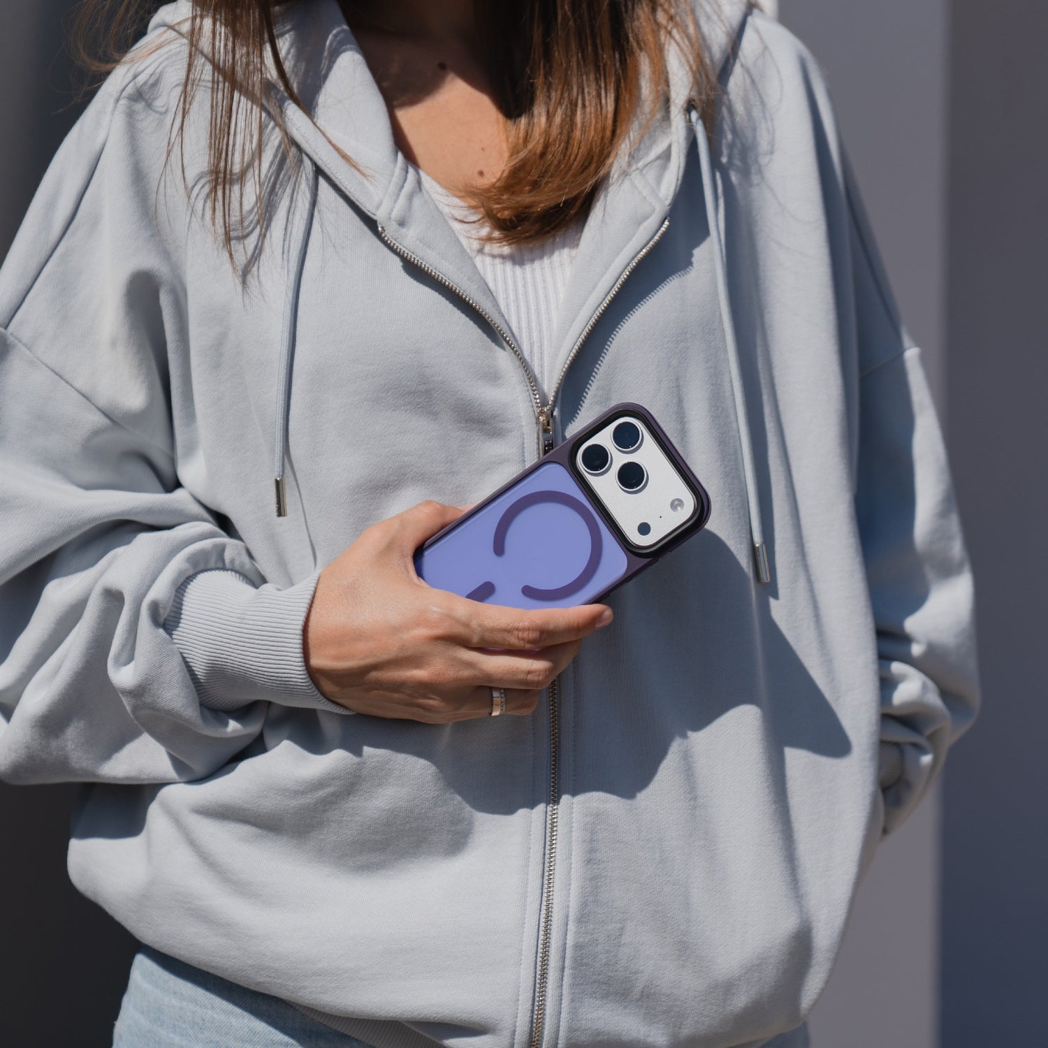 Eine Frau im hellgrauen Kapuzenpulli hält ihr Arktis iPhone 17 Pro Solid Case mit MagSafe, eine mattlila Schutzhülle, während sie draußen steht.