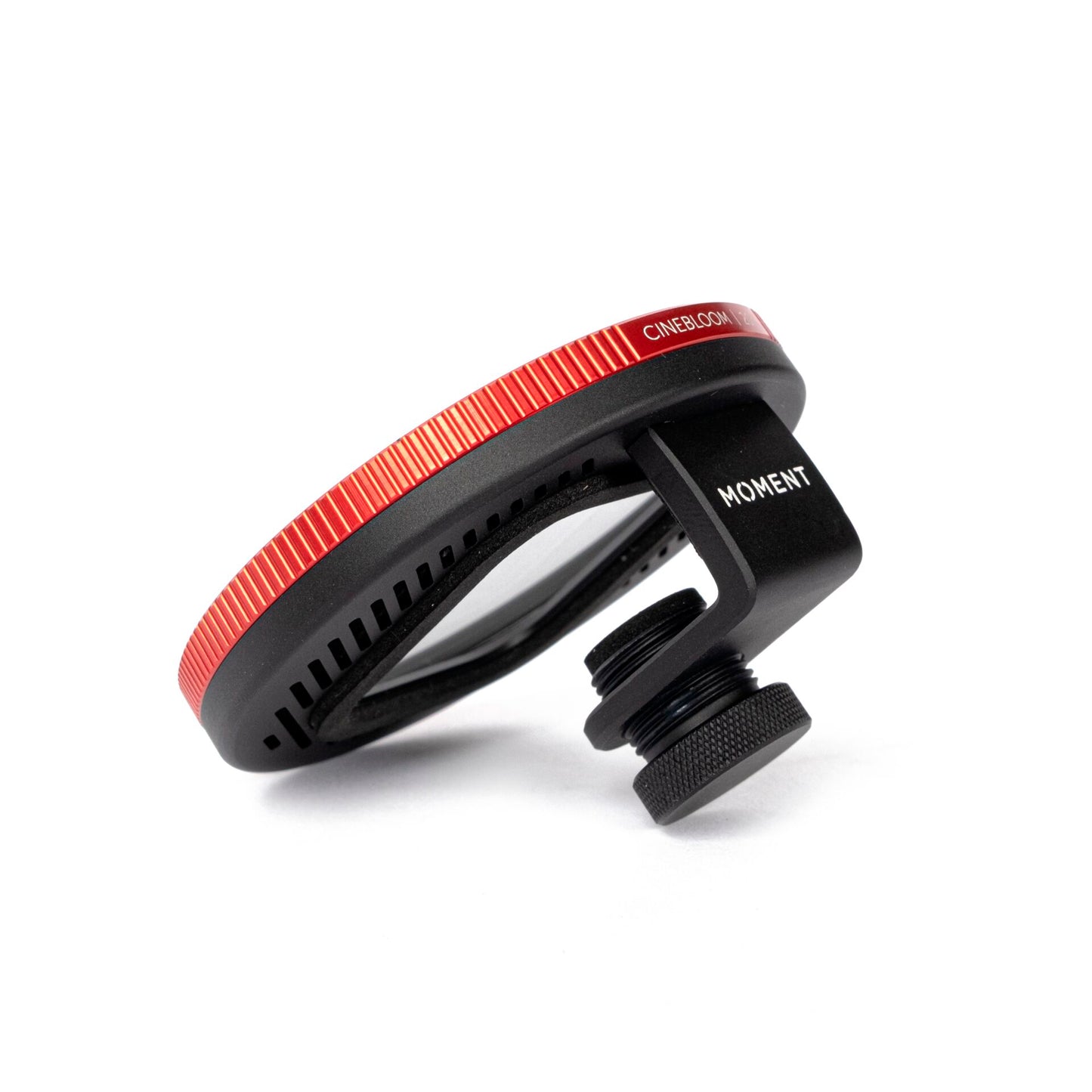 Nahaufnahme des MOMENT 67 mm Universal Phone Case kompatibler Filter Mount, der mit einem roten Ring und einer schwarzen Klemme an einem Kameraobjektivfilter befestigt ist, dargestellt vor einem weißen Hintergrund.