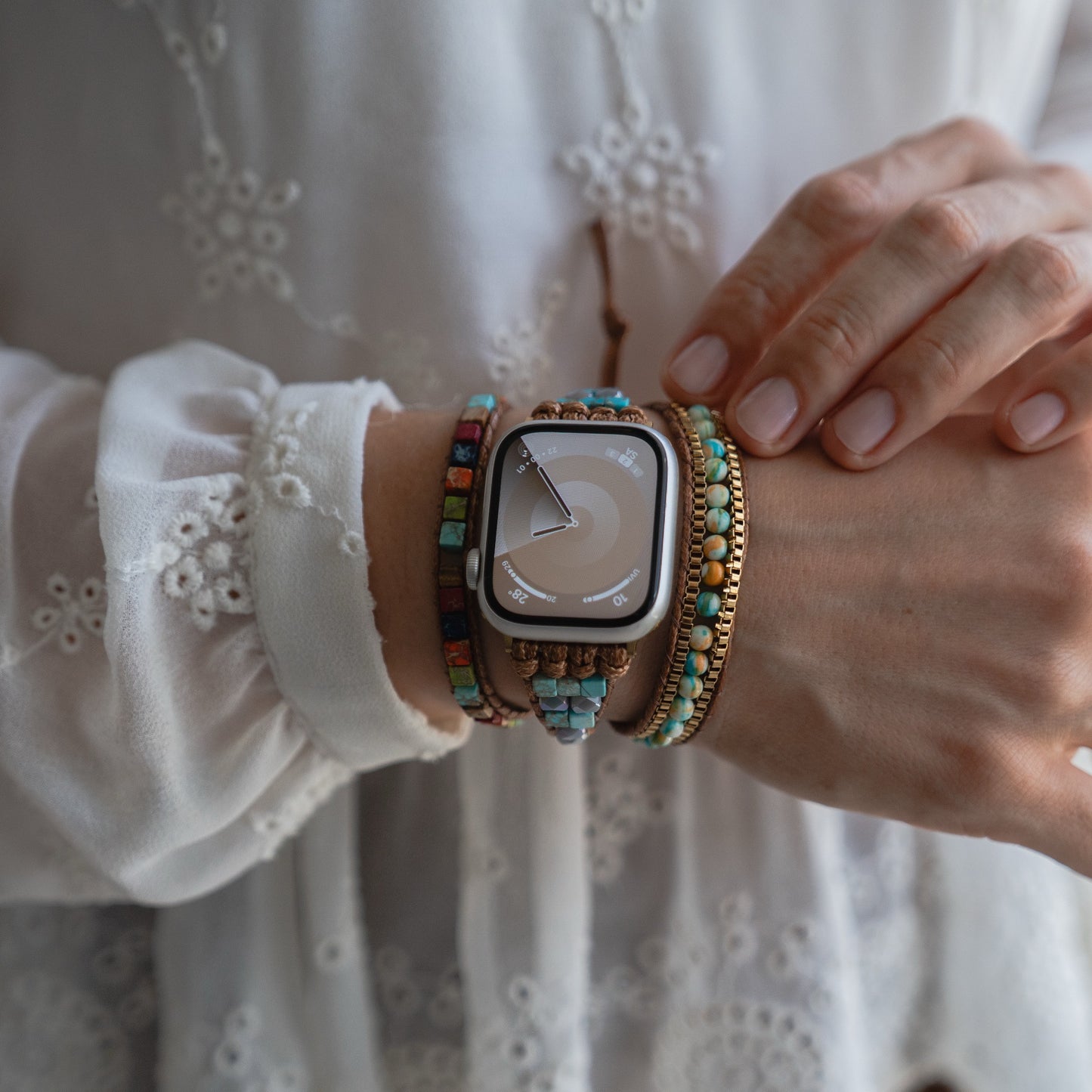 Eine Person trägt ein arktisband Apple Watch Armband "Dream Catcher" von arktisband, gepaart mit bunten Perlenarmbändern und einer weißen bestickten Bluse.