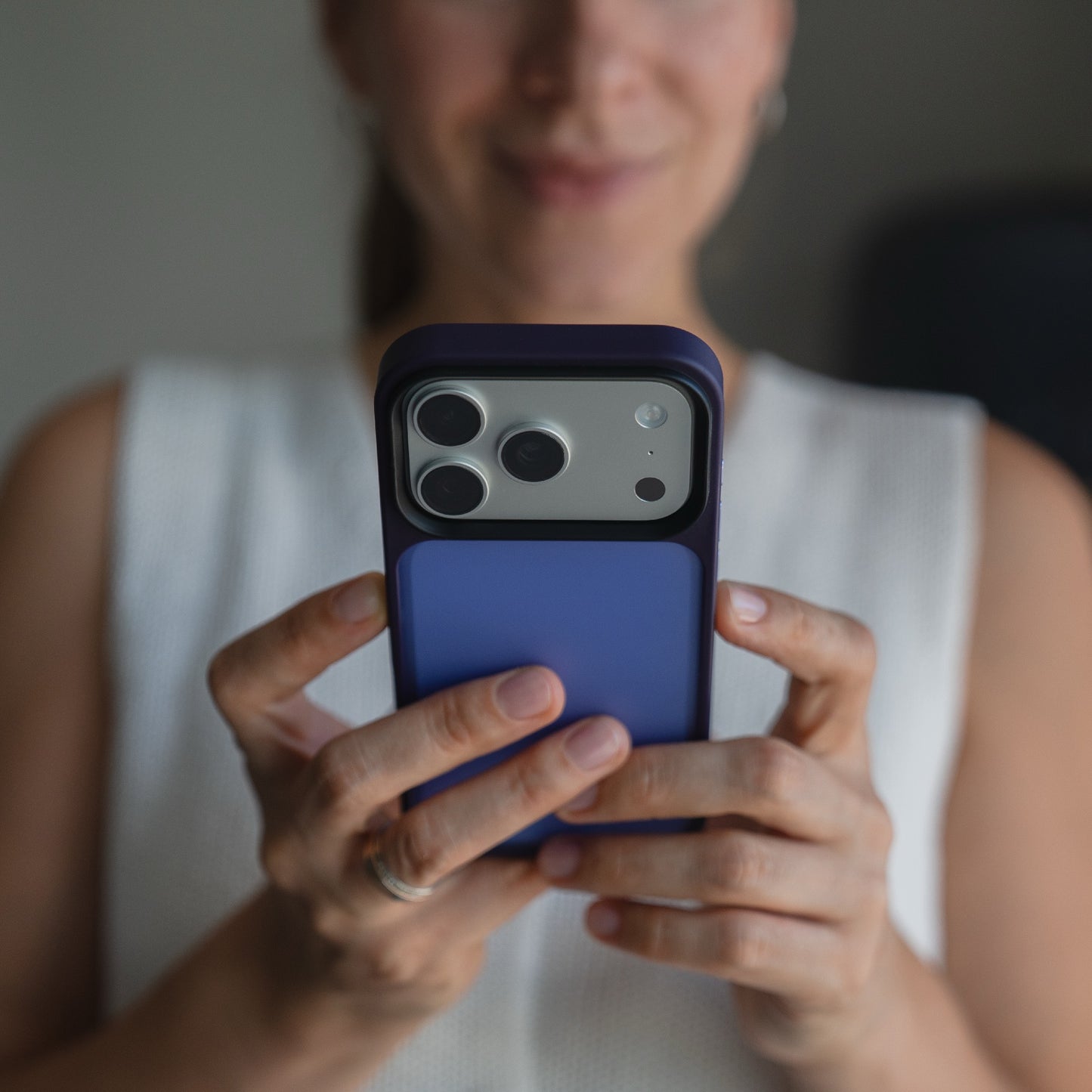 Eine Frau, von den Schultern aufwärts gesehen, hält ihr Smartphone geschützt durch das Arktis iPhone 17 Pro Solid Case in mattem Blau und lächelt leicht.