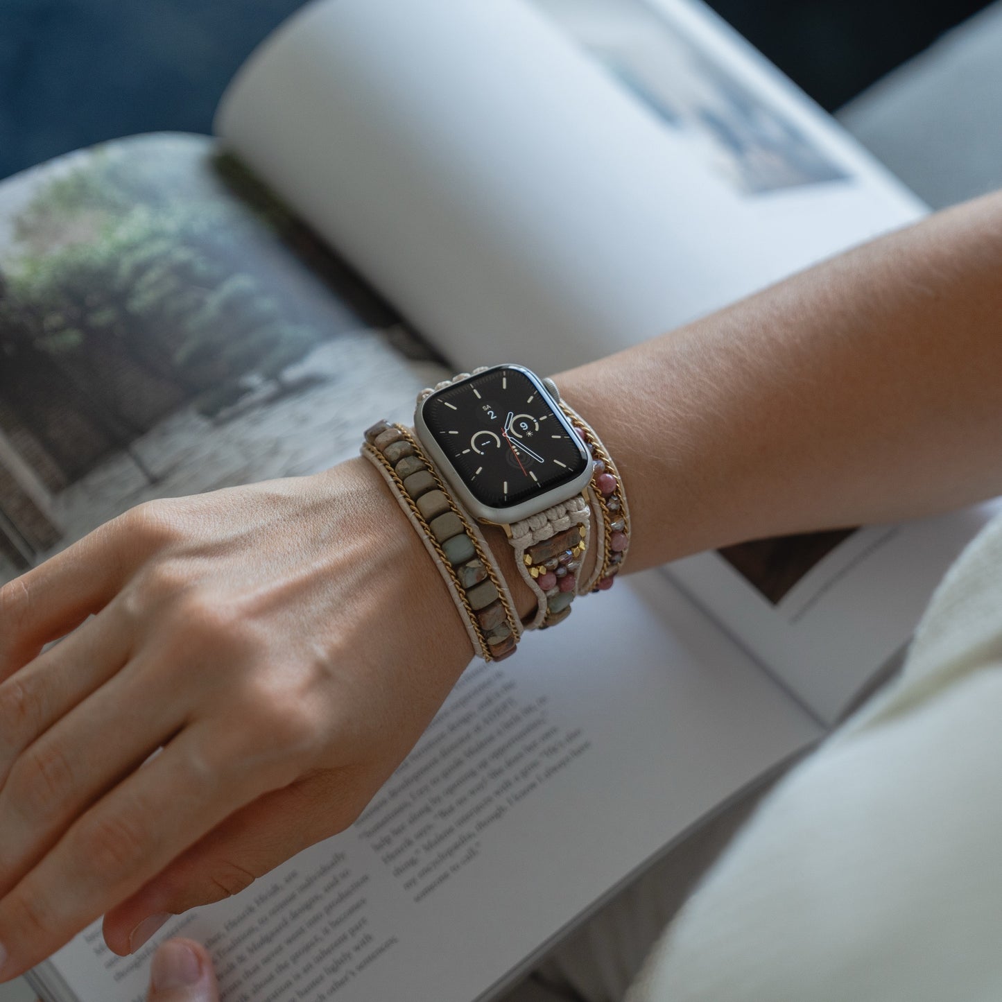 Eine Person, die ein Boho-Armband und das arktisband Apple Watch Armband "Dream Catcher" von arktisband trägt, liest eine Zeitschrift mit einem bezaubernden Naturfoto.
