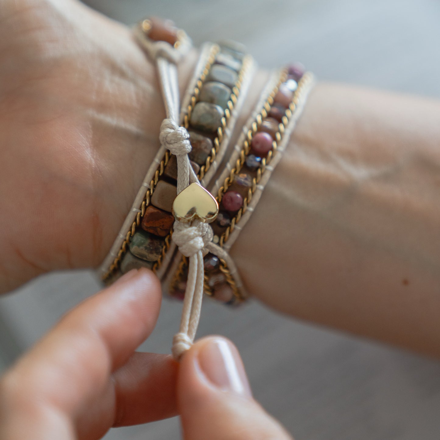 Eine Hand bindet ein stilvolles Boho-Arktisband Apple Watch Armband "Dream Catcher" mit einem goldenen Herzanhänger um das Handgelenk und kombiniert es mühelos zu einem schicken Lagenlook.