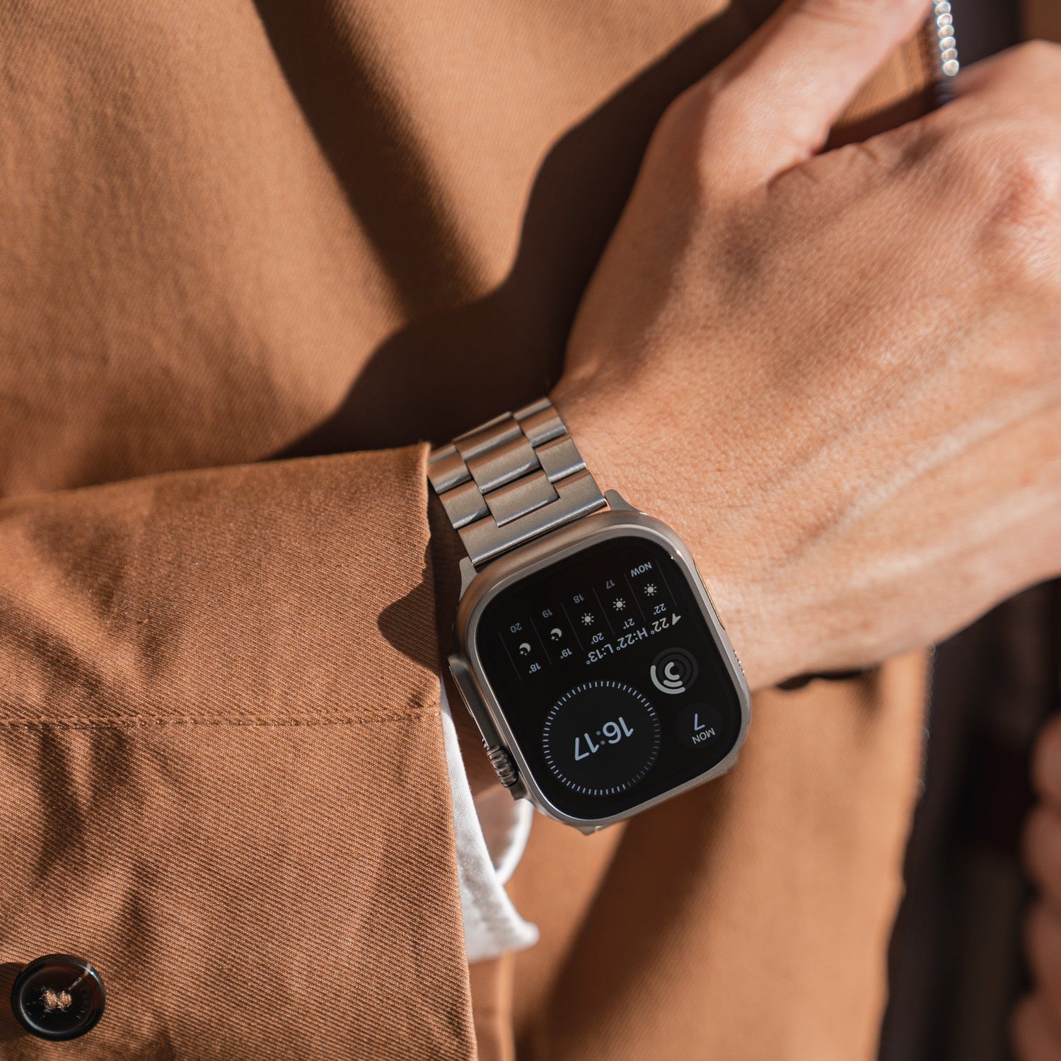 Eine Person, die einen braunen Mantel und ein arktisband Apple Watch Gliederarmband „Arctica“ von arktisband mit einem rechteckigen Display mit Uhrzeit, Datum und Symbolen trägt, präsentiert die Uhr elegant an ihrem linken Handgelenk.