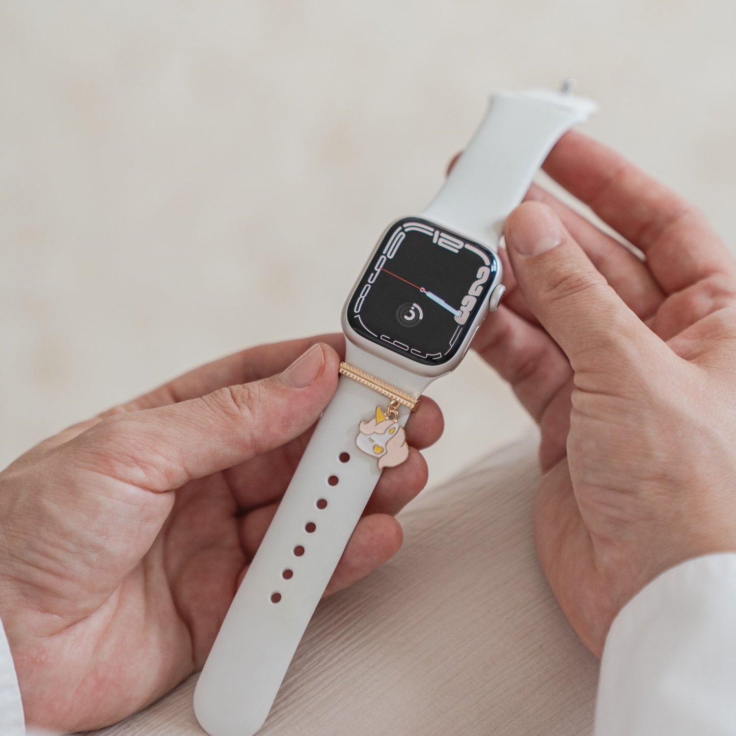 Eine Person in einem weißen Langarmhemd hält eine weiße Apple Watch mit rechteckigem Zifferblatt, an deren Armband als exklusives Accessoire ein arktisband Apple Watch Armband Charm von arktisband befestigt ist.