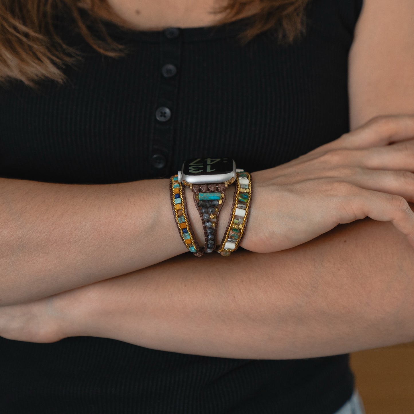 Eine Person mit verschränkten Armen trägt ein schwarzes Top, das arktisband Apple Watch Armband "Dream Catcher" von arktisband und bunte Boho-Armbänder.