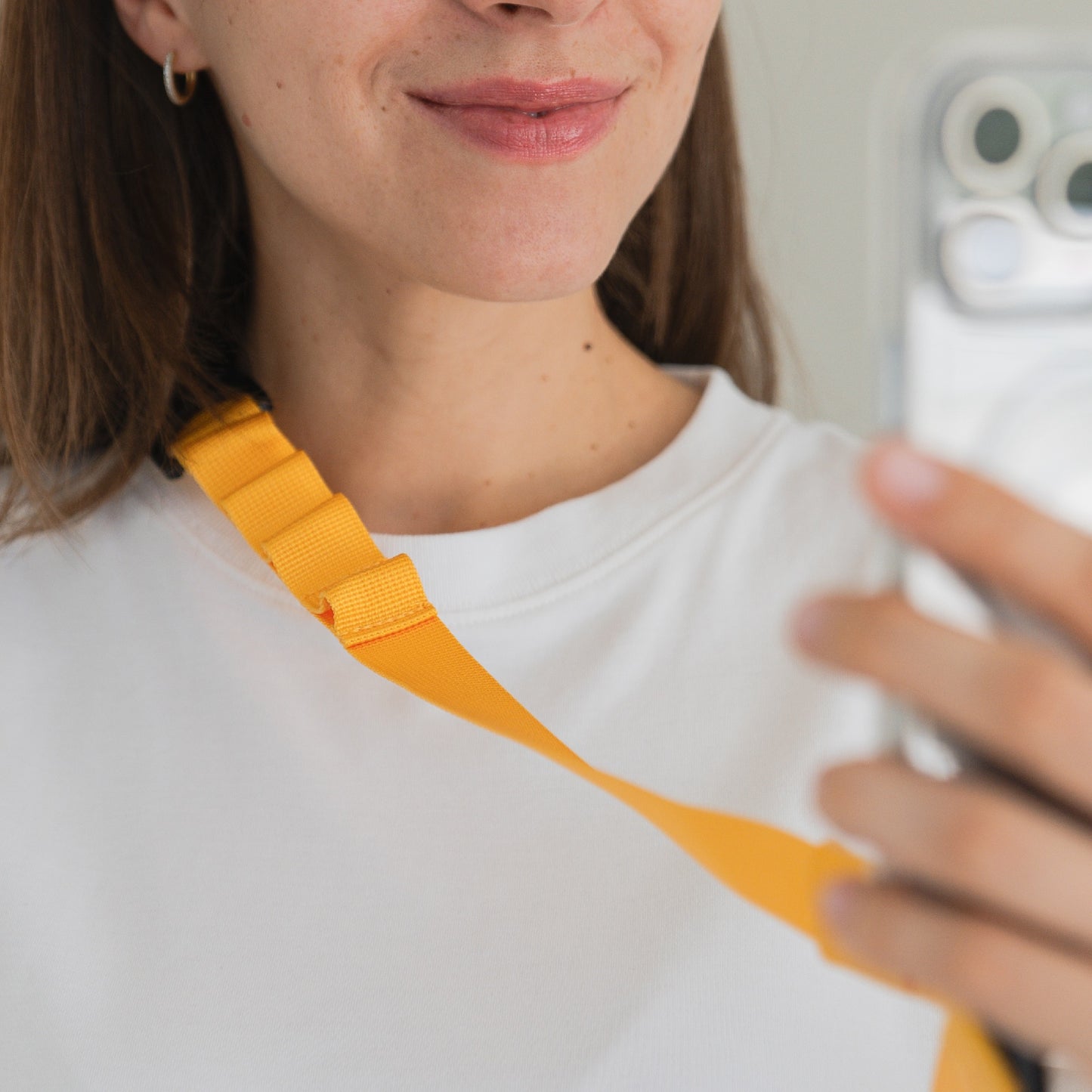 Eine Frau mit weißem Hemd und dem gelben arktis Smartphone-Gurtband-Lanyard macht ein Spiegel-Selfie, auf dem nur die untere Hälfte ihres Gesichts und die Hand zu sehen sind, die ihr Telefon hält.