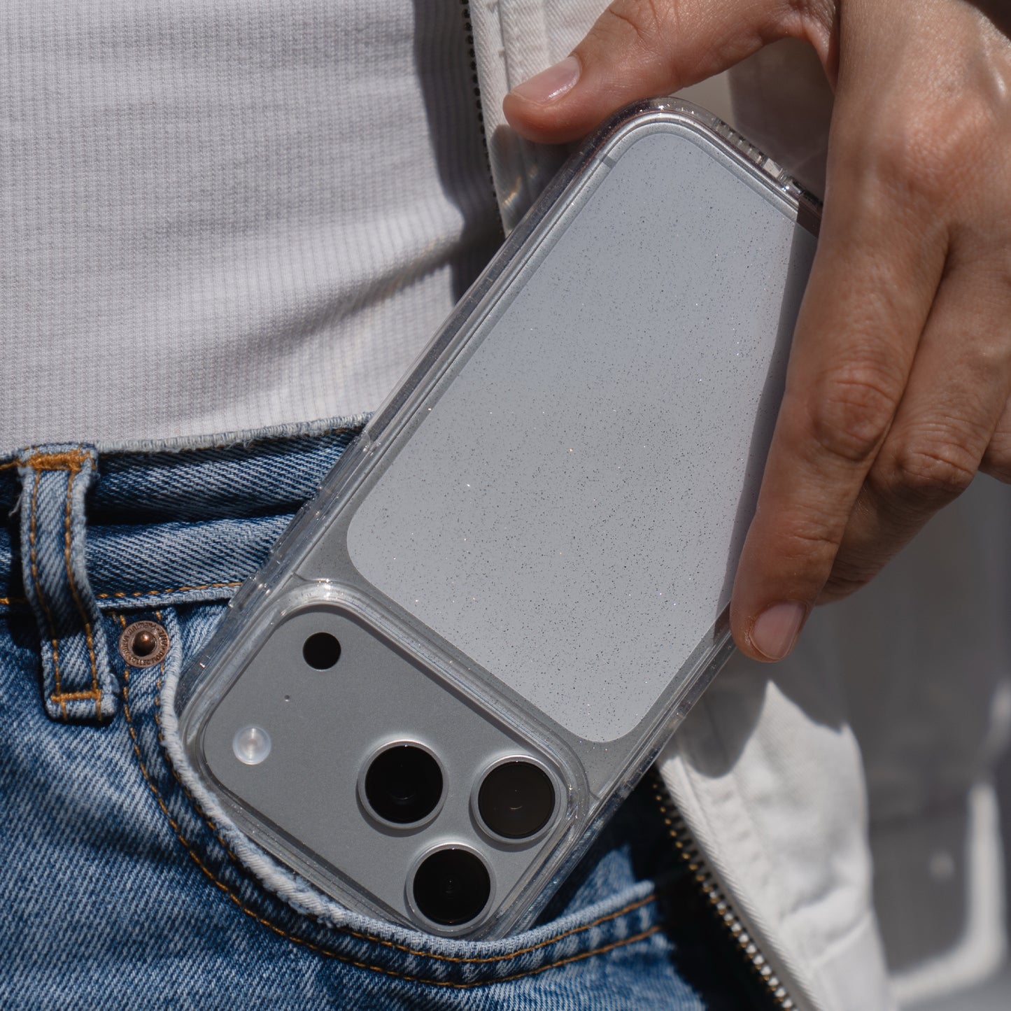 Eine Hand schiebt ein arktis iPhone 17 Pro Max Glitter Case in die Vordertasche einer Blue Jeans.