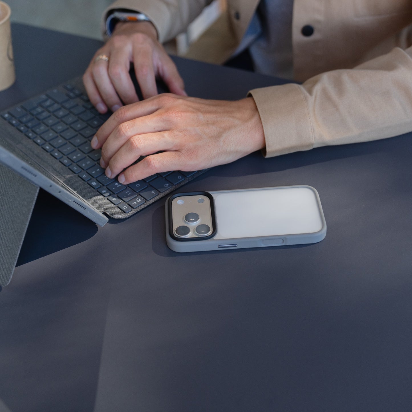 Eine Person, die an einem Schreibtisch auf einem Laptop tippt, mit einem Arktis iPhone 17 Pro Solid Case, das für sein mattes und stoßabsorbierendes Design bekannt ist, neben ihren Händen.