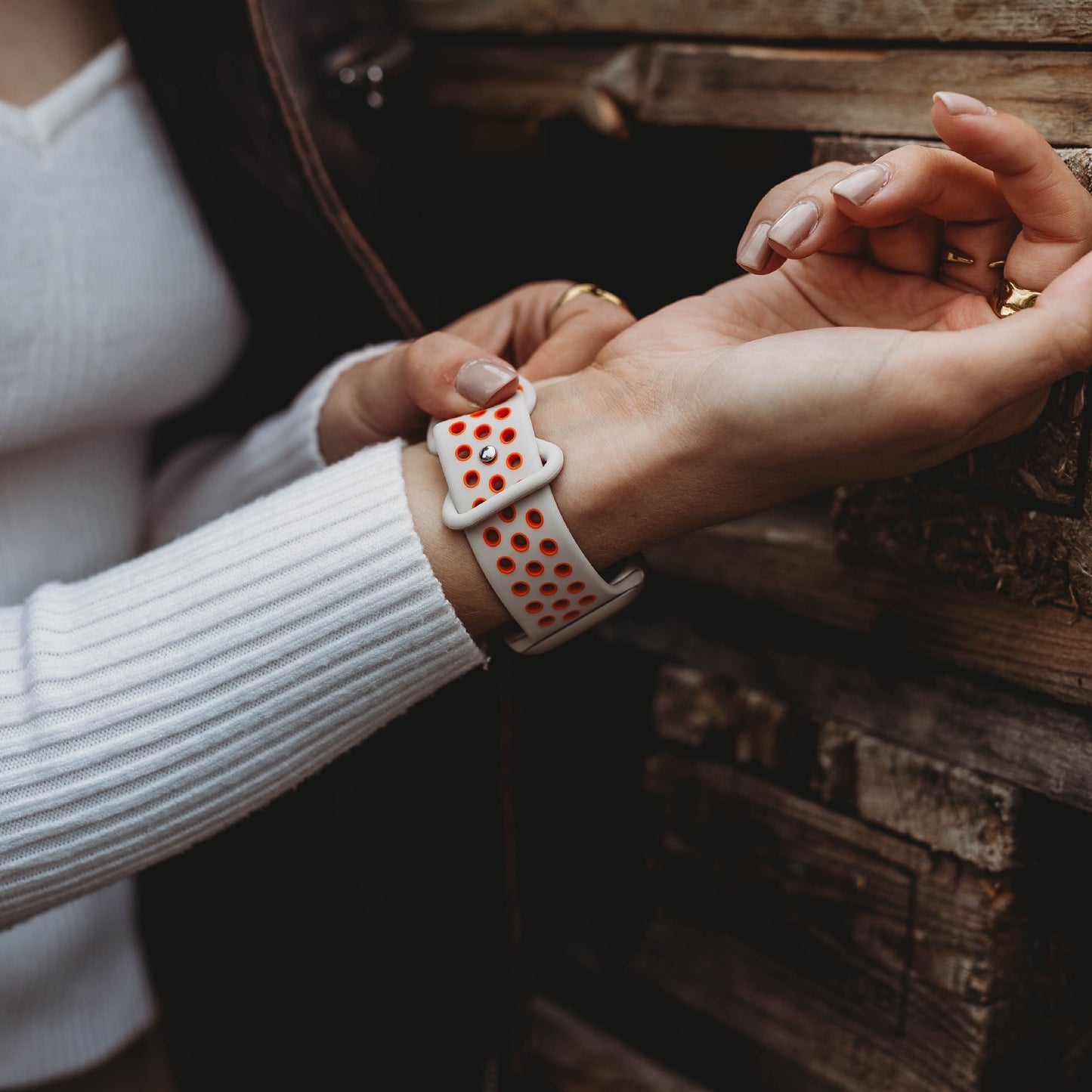 Eine Person in einem weißen gerippten Langarmshirt rückt vor einer Holzwand ein Arktisband Apple Watch Silikonarmband „Energy“ mit roten Löchern an ihrem Handgelenk zurecht.