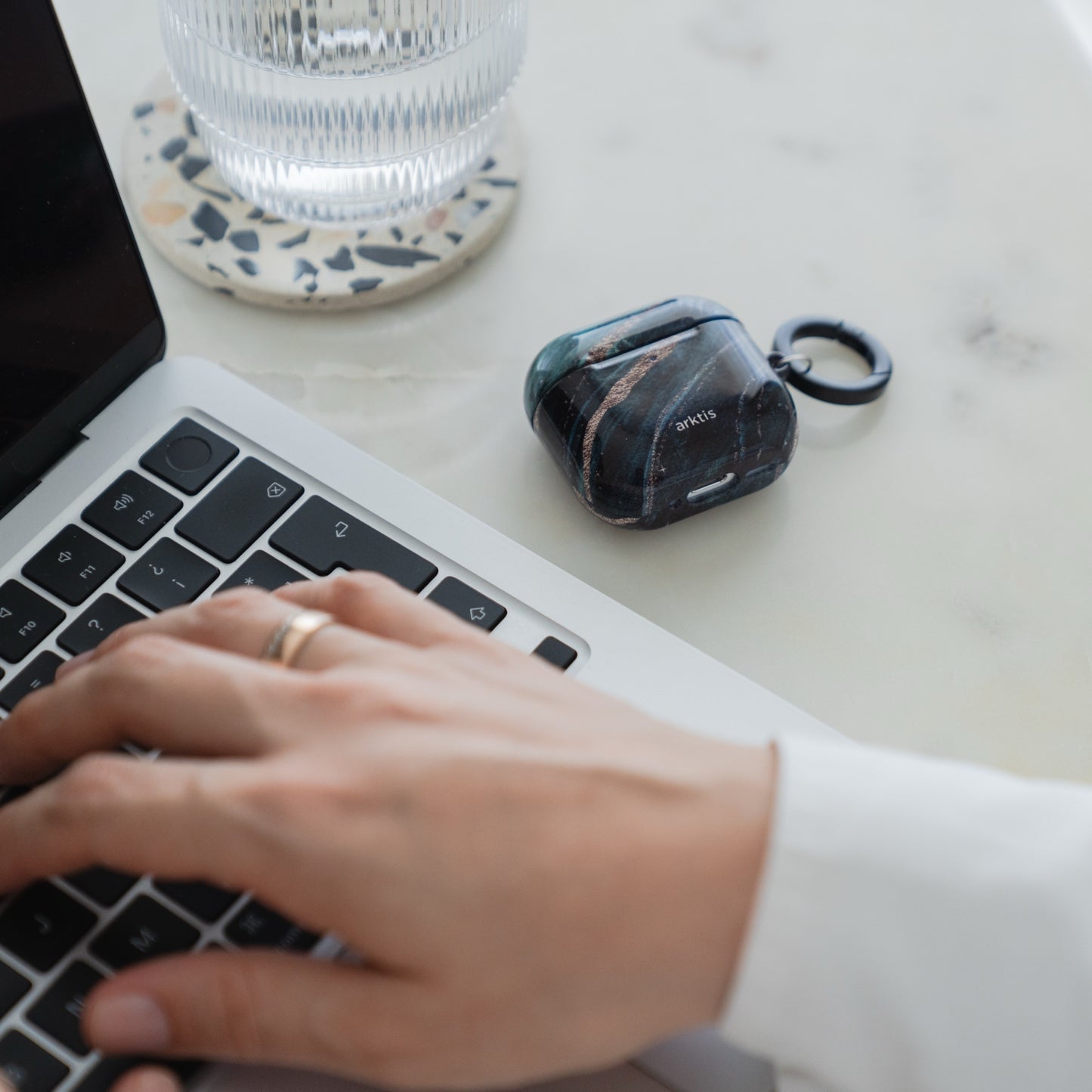 Arktis AirPods 5 Hülle – Green Marble-Hülle mit grün-schwarzem Marmormuster, die auf einem Schreibtisch neben einem Laptop liegt.