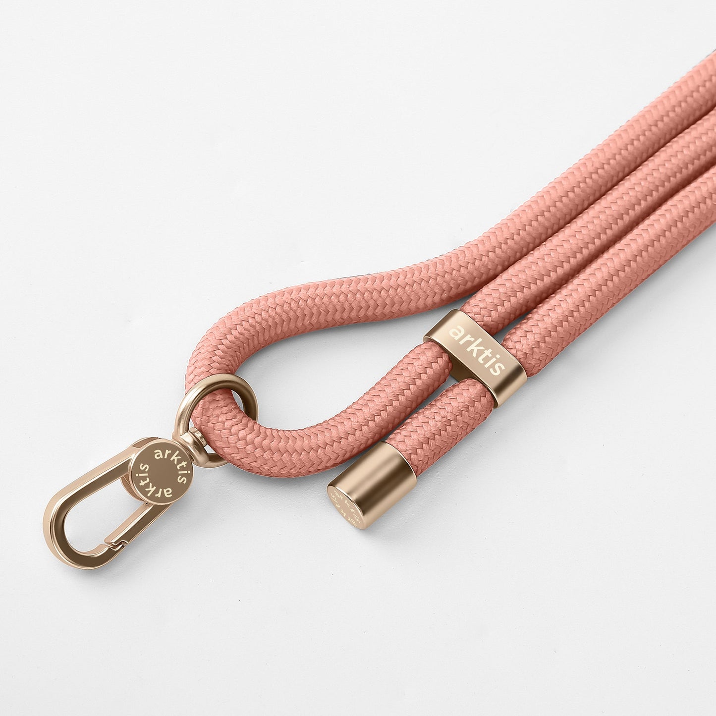 Die arktis Lanyard Handykette fürs Handgelenk von Arktis besteht aus einem pfirsichfarbenen geflochtenen Seil mit goldenen Metallakzenten, einschließlich eines Verschlusses und eines Rings mit Markengravur, und präsentiert sich als ideales Smartphone-Zubehör auf weißem Hintergrund.