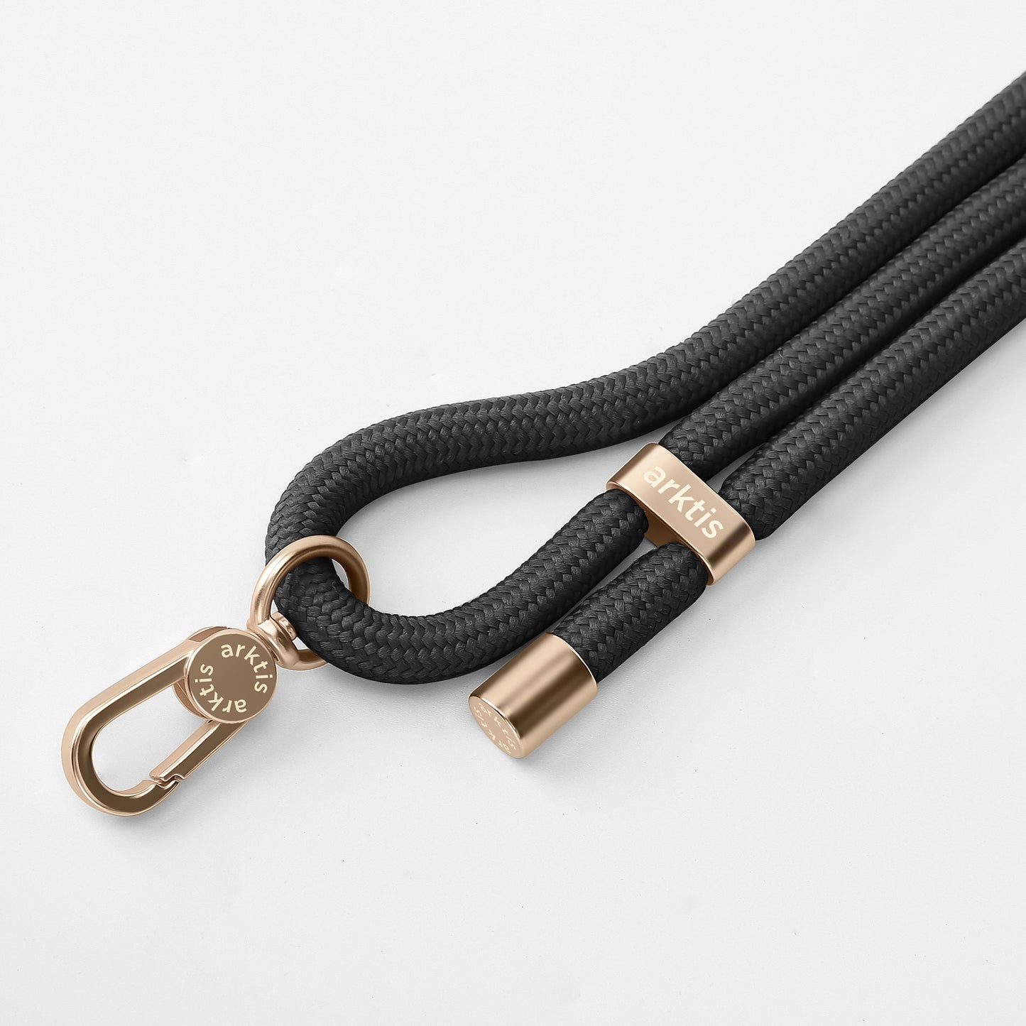 Eine Nahaufnahme der Arktis Lanyard Handykette fürs Handgelenk von Arktis mit einer schwarzen geflochtenen Kordel mit goldenen Enden und einem Verschluss mit eingraviertem Markennamen auf weißem Hintergrund – ideal als stilvolles Smartphone-Zubehör.