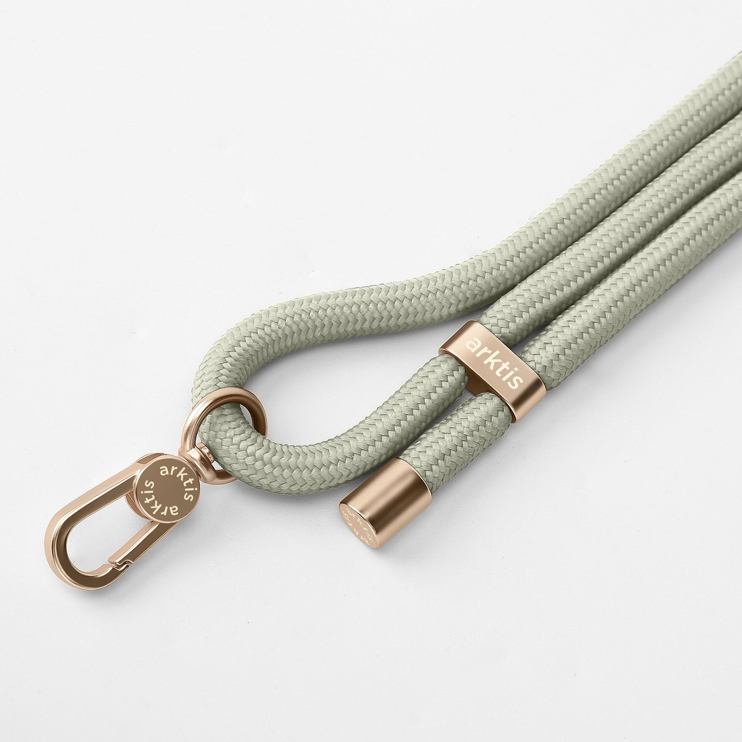 Eine Nahaufnahme der Arktis Lanyard Handykette fürs Handgelenk von Arktis mit einer hellgrauen geflochtenen Kordel mit roségoldenen Metallakzenten und einem gravierten Verschluss auf weißem Hintergrund – ein stilvolles Smartphone-Accessoire.