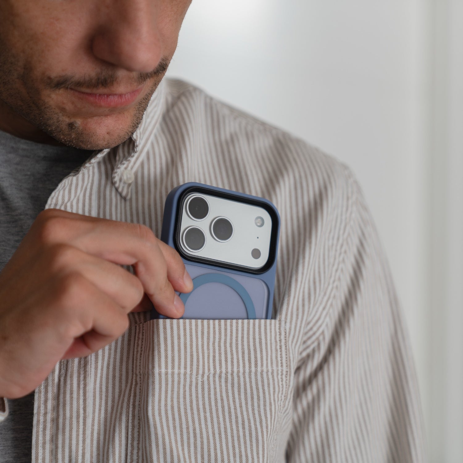Ein Mann steckt ein iPhone 17 Pro mit der arktis iPhone 17 Pro Solid Case mit MagSafe von Arktis in die Brusttasche seines gestreiften Hemds - die matte Hülle schützt das Gerät stilvoll im Alltag und ist MagSafe-kompatibel.