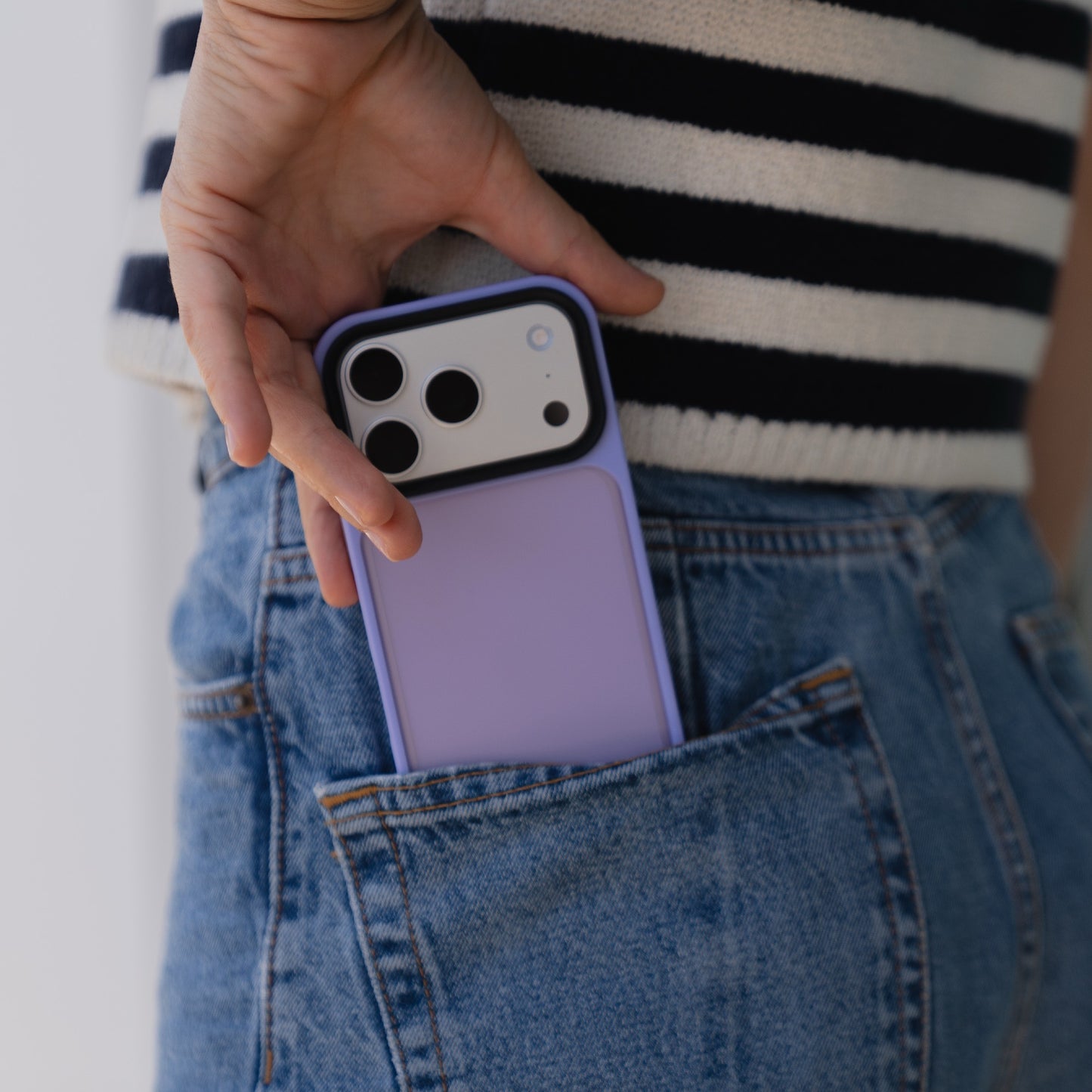 Eine Person steckt ein lavendelfarbenes iPhone mit einem Arktis iPhone 17 Pro Solid Case in die Gesäßtasche einer blauen Jeans.