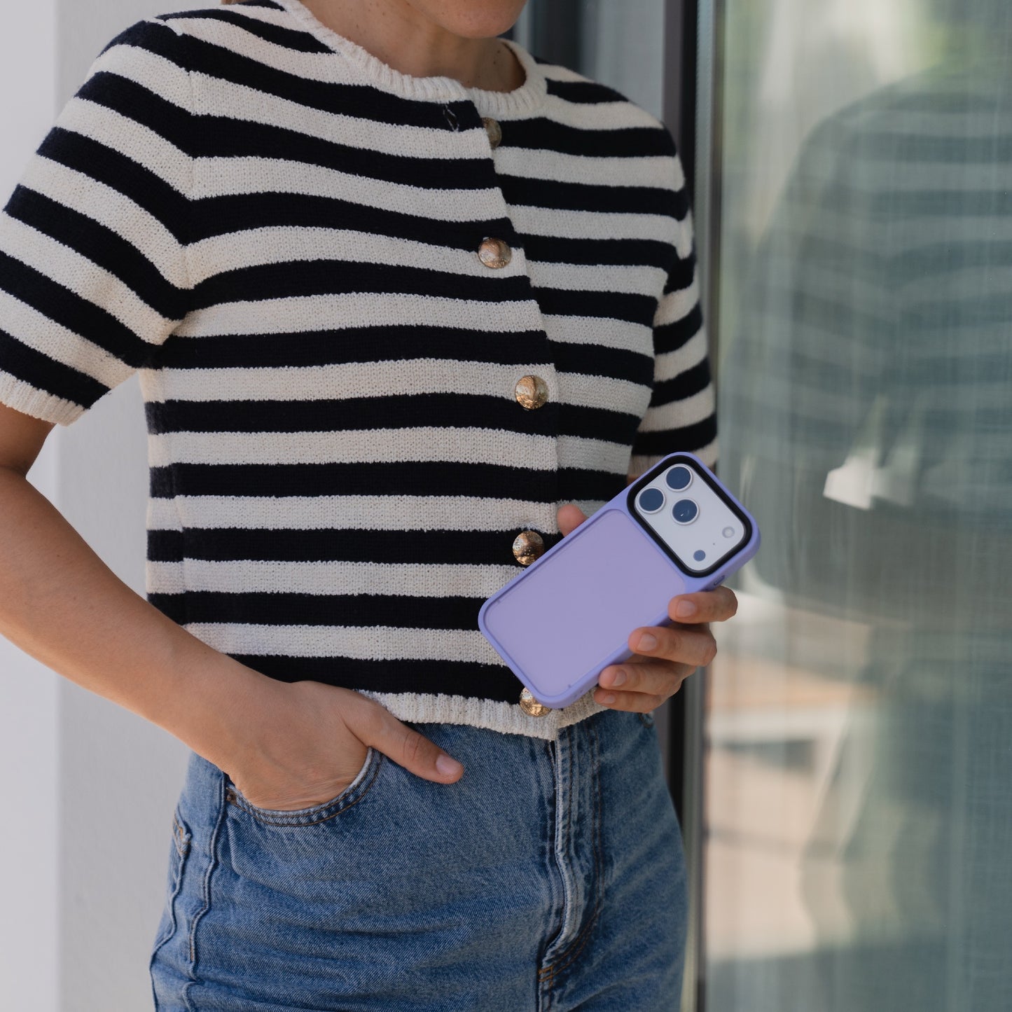 Eine Person in gestreiftem Hemd und Jeans hält ein Arktis iPhone 17 Pro Solid Case neben einer Glastür.