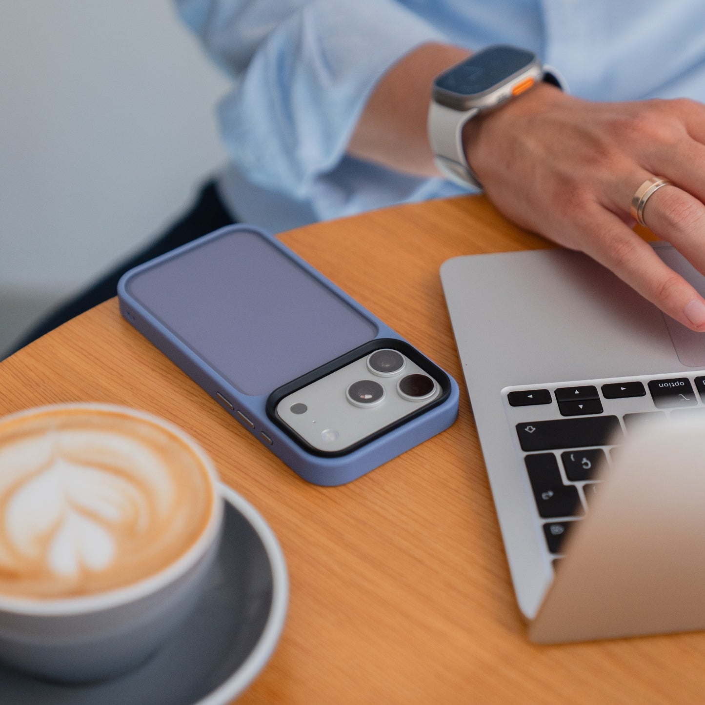 Eine Person benutzt einen Laptop an einem Tisch mit Kaffee und einem Smartphone in einem Arktis iPhone 17 Pro Solid Case (blau) von Arktis in der Nähe.