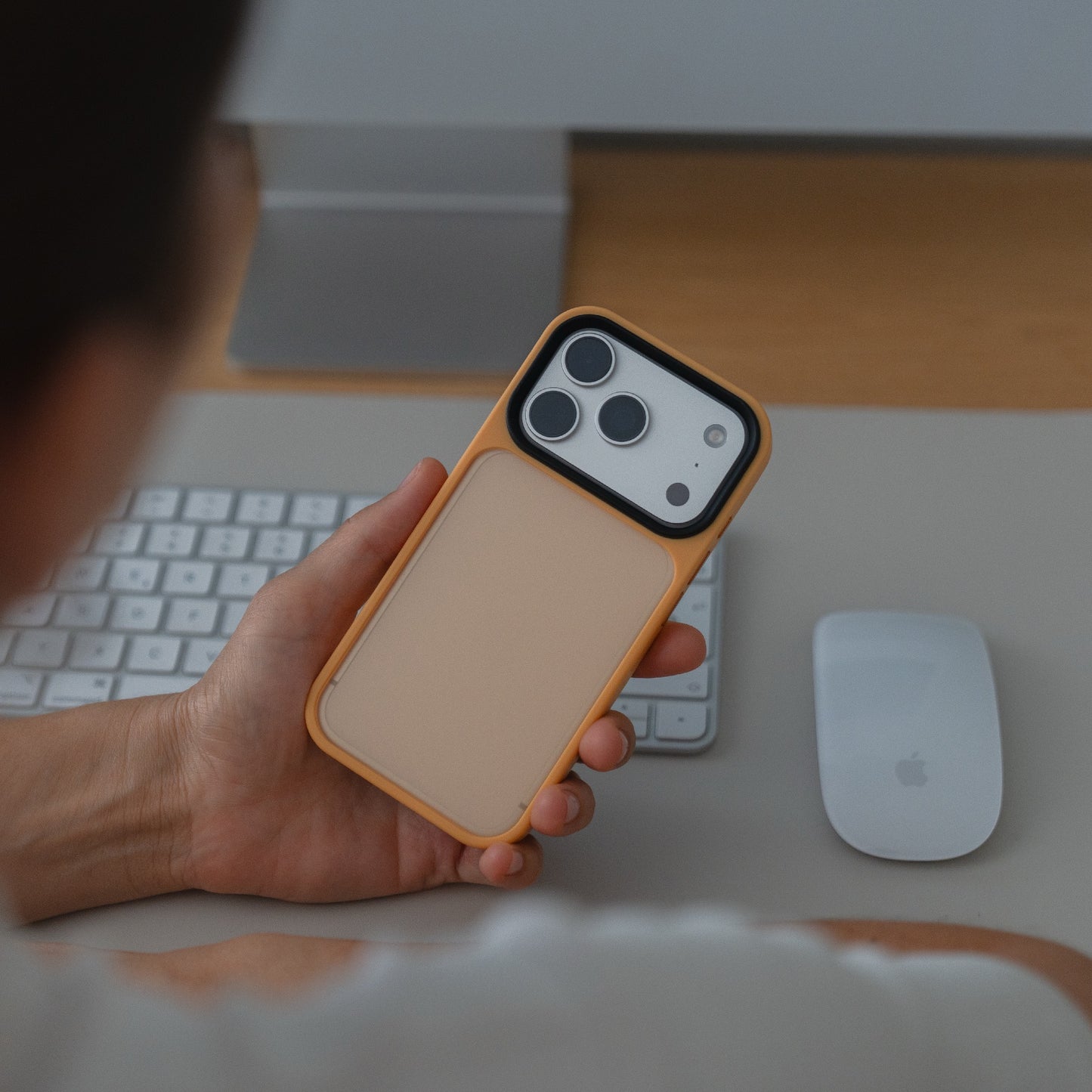 Eine Person hält eine Arktis arktis iPhone 17 Pro Solid Case mit stoßabsorbierendem TPU-Silikon und mattem Finish am Schreibtisch mit Tastatur und Apple Magic Mouse.