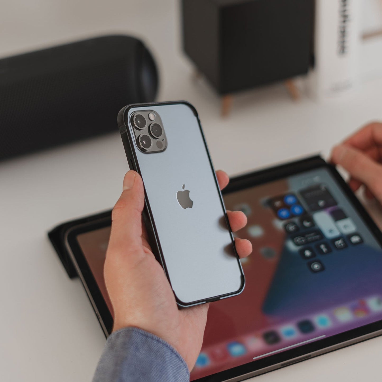 Eine Hand hält ein iPhone mit dem arktis iPhone Air Bumper von arktis neben einem iPad mit Kontrollzentrum auf einem Schreibtisch.