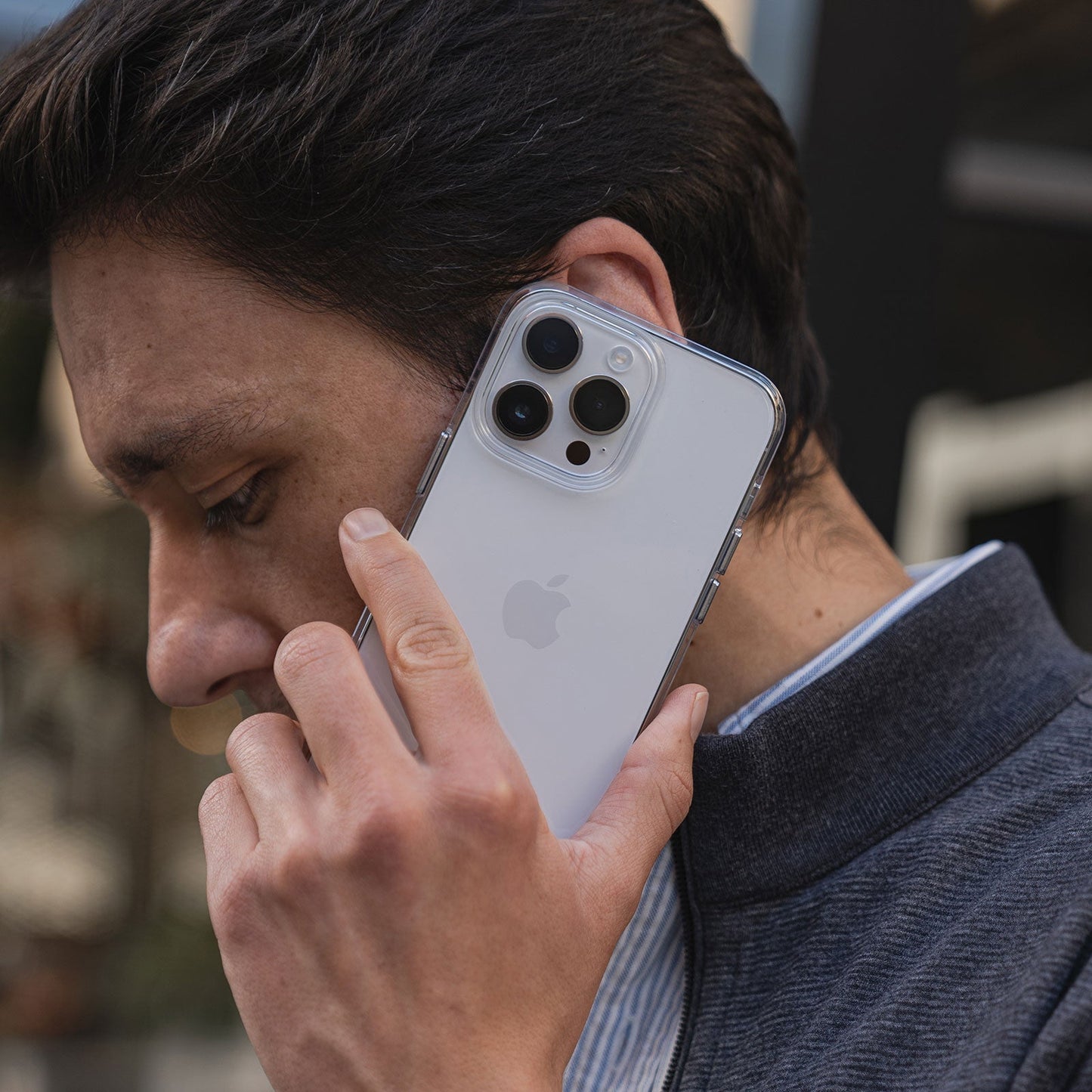 Eine Person hält ein weißes iPhone 15 Pro Max mit drei Kameras in einem MR PROTECT iPhone 15 Pro Max CLEAR Case an ihr Ohr und scheint zu telefonieren.