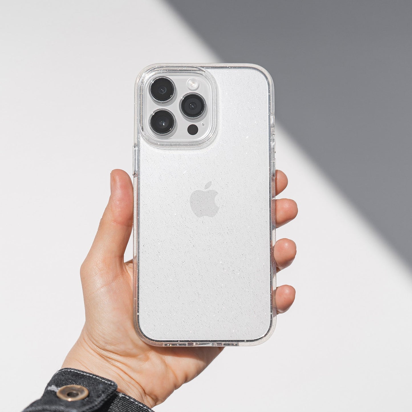 Eine Hand hält das Blingmeister iPhone 15 Pro Max CRYSTAL GLITTER Case, das vor Kratzern schützt, vor einem weiß-grauen Hintergrund.