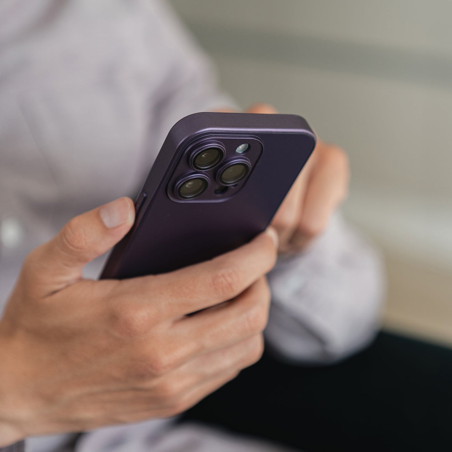 Eine Person hält ein Arktis iPhone 16 Tech Case in Dunkelviolett, das den Dreifachkameraschutz des Cases hervorhebt. Zu sehen sind lediglich ihre Hände, ein Teil des Telefons und ein helles Hemd.